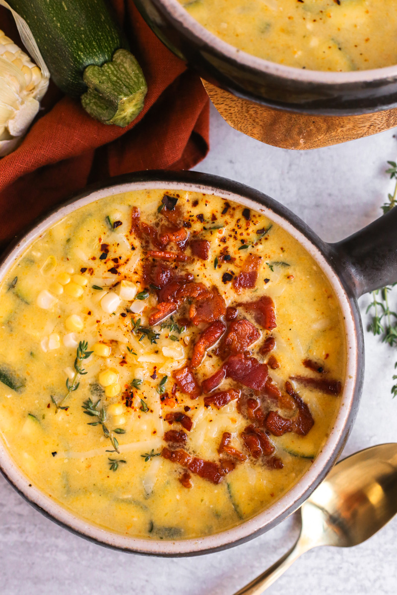 Close up view of a creamy corn chowder recipe, served with bacon bits, cheese, and fresh thyme