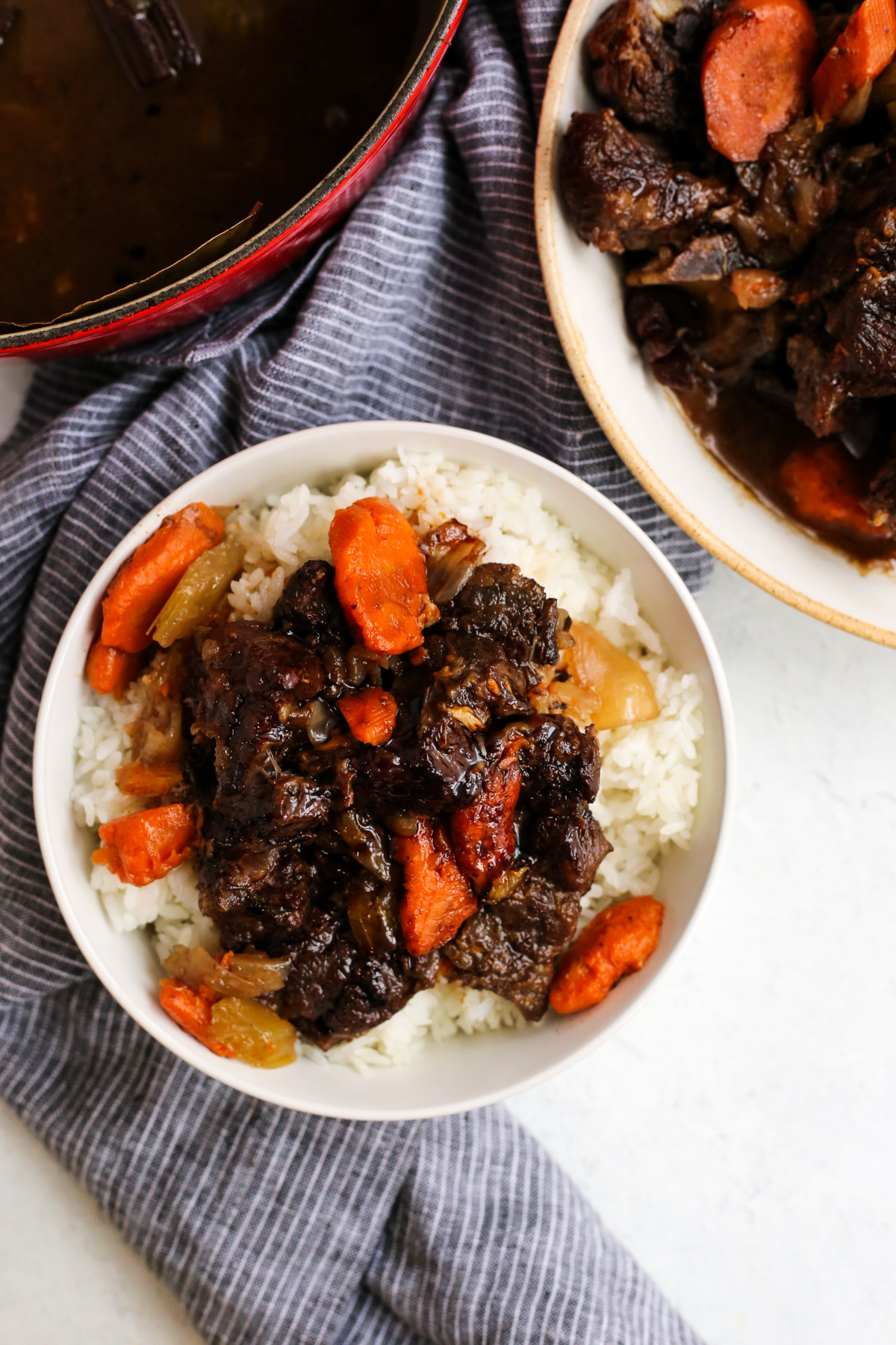 Overhead view of a braised beef recipe served with white rice, served on a kitchen countertop with the rest of the recipe featured in the shot