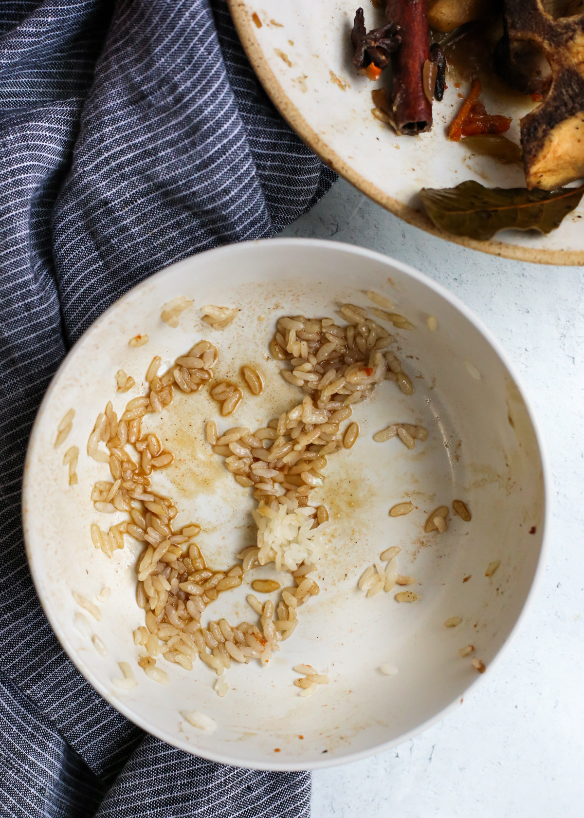An empty ceramic bowl with remnants of white rice, spices, and a braising liquid 