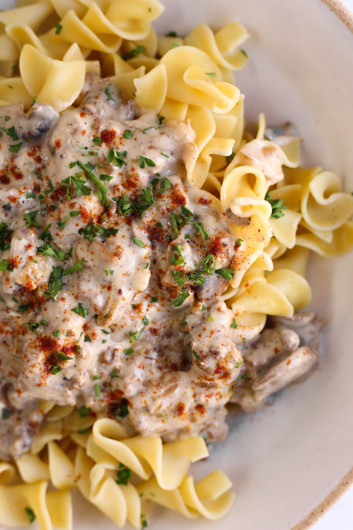 Close up view of a ground beef stroganoff recipe served on top of egg noodles in a ceramic bowl