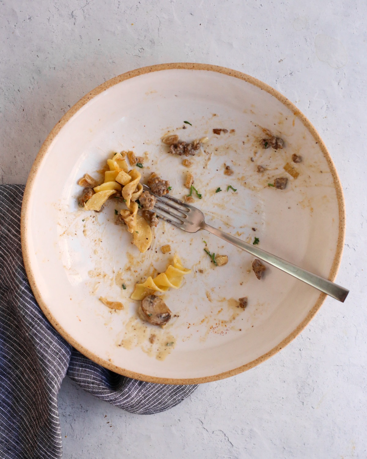 Overhead view of an empty ceramic bowl that shows all of the ground beef stroganoff recipe has been eaten, with a few noodles and a fork left in the bowl