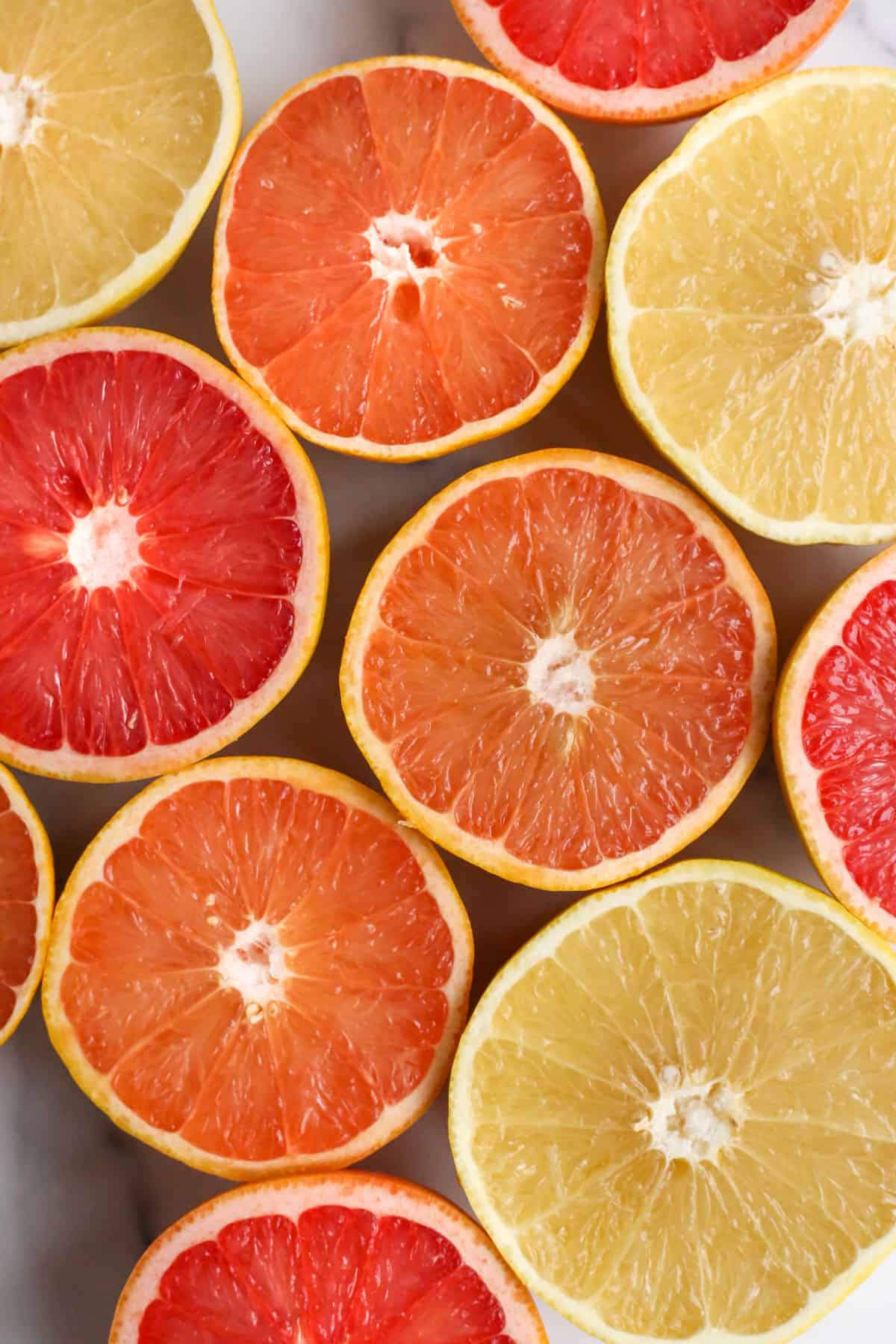 Flatlay of sliced grapefruit, sliced sides facing up, arranged on a kitchen countertop with varying colors from yellow to orange to ruby red