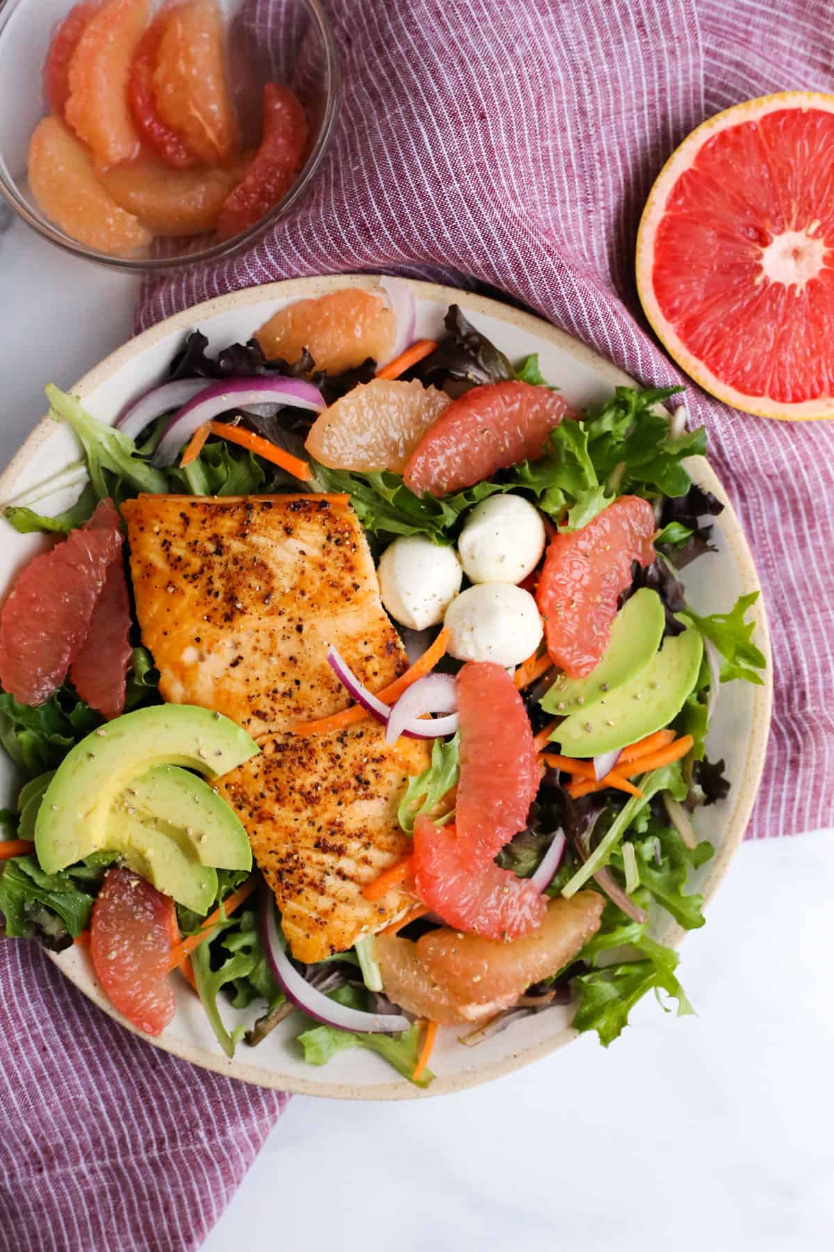 Overhead view of a simple grapefruit salad with seared salmon and sliced veggies, served on a ceramic dish on a kitchen counter, surrounded by fresh grapefruit segments