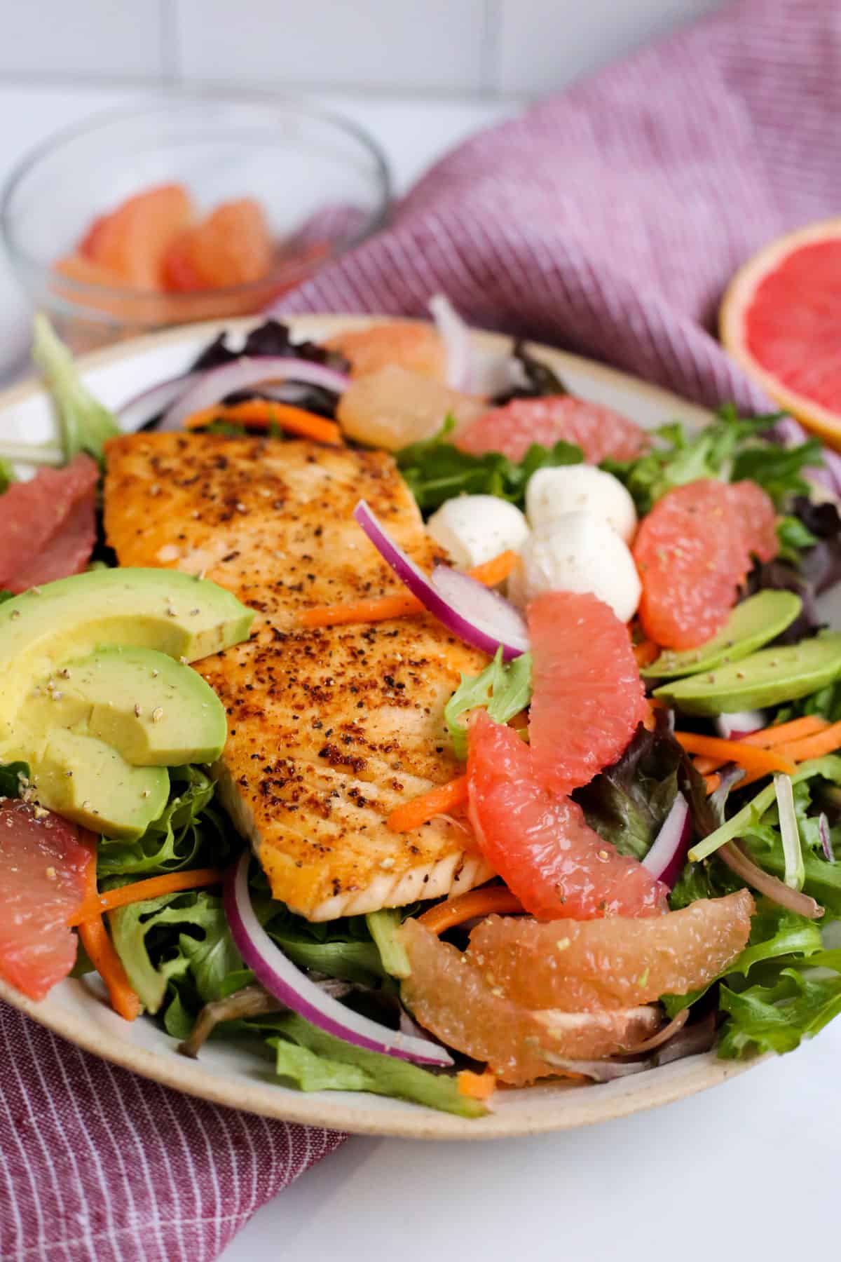 A colorful salad served on a ceramic dish, featuring seared salmon, grapefruit wedges avocados, and other ingredients that complement grapefruit nutrition and flavor