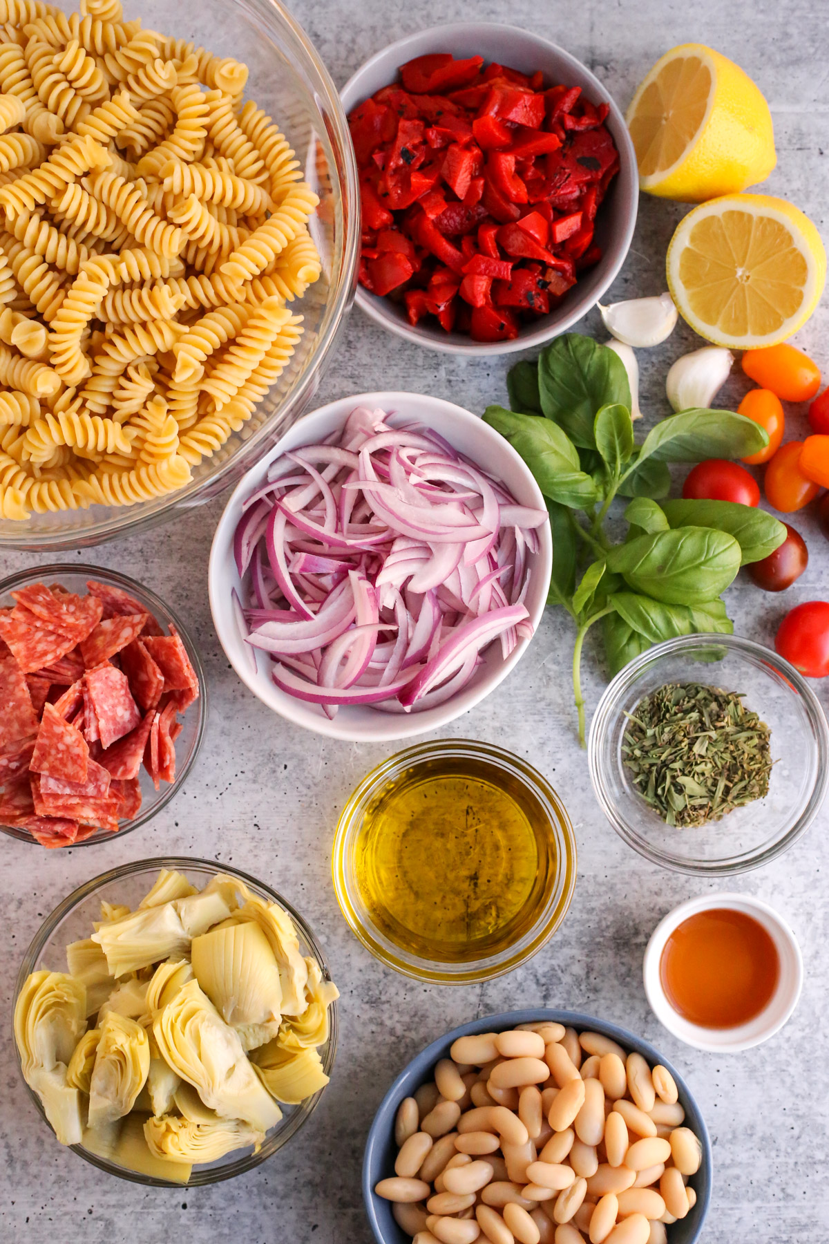 An assortment of ingredients for antipasto pasta salad, displayed in a flat lay style using small ceramic bowls and ramekins 