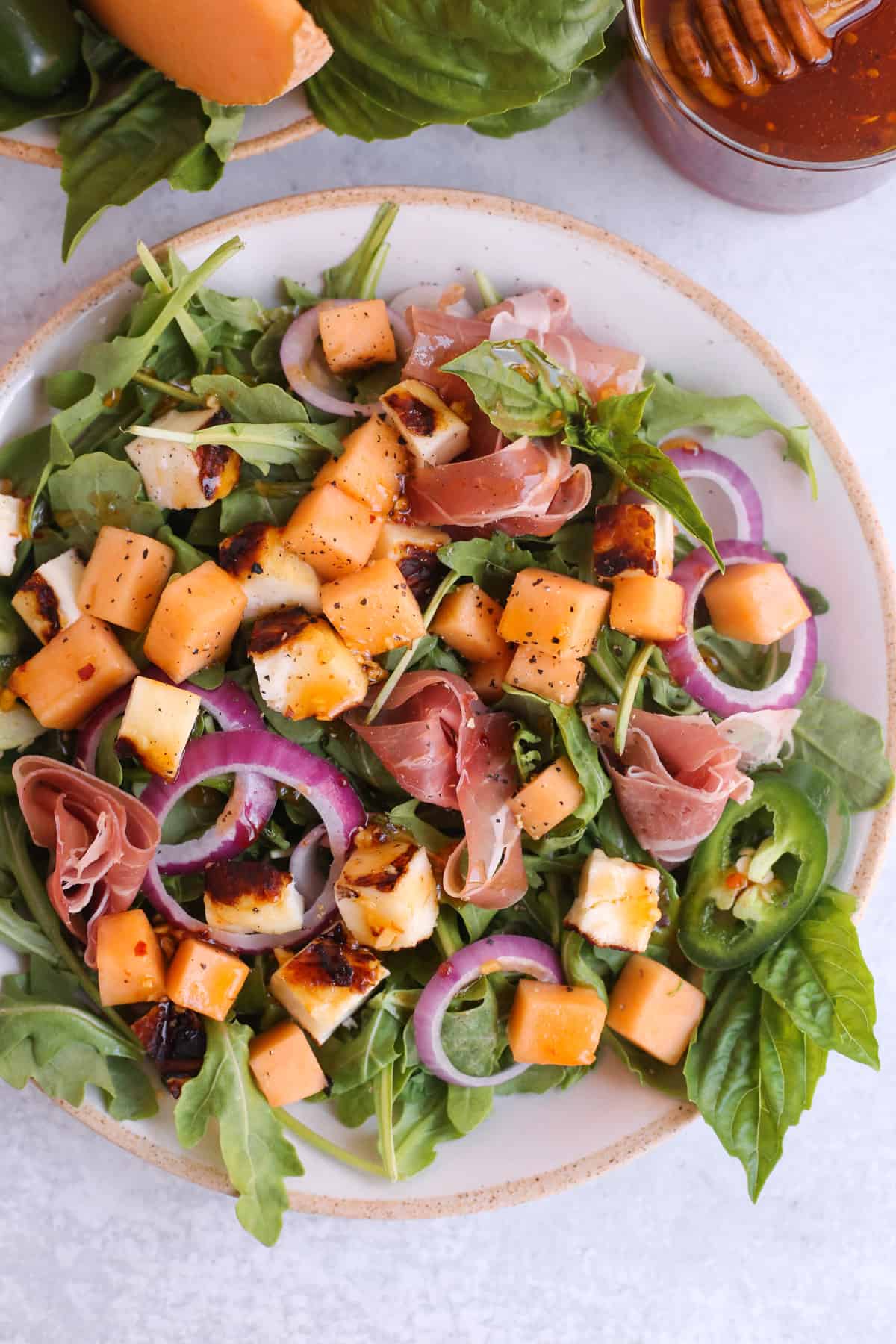Close crop overhead view of a colorful salad featuring halloumi cheese, chopped cantaloupe, prosciutto, red onion, and fresh basil and cracked black pepper on top