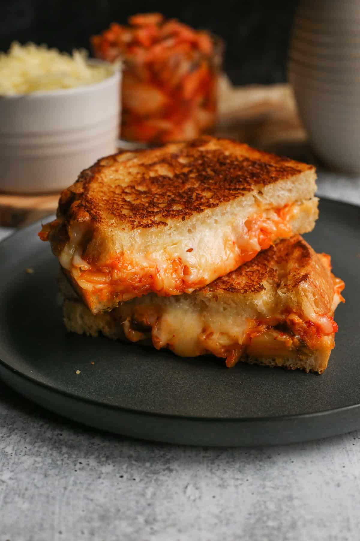 Close up view of a kimchi grilled cheese sandwich, sliced in half and stacked to reveal the melted cheese and kimchi inside the toasted sourdough bread