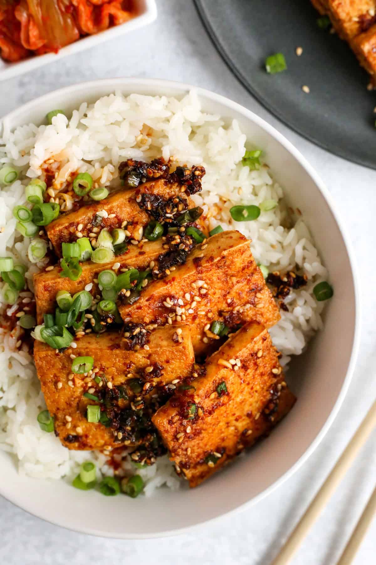 Overhead view of a bowl of white rice topped with dubu jorim, Korean spicy braised tofu, garnished with lots of sliced green onions, sesame seeds, and a flavorful sauce