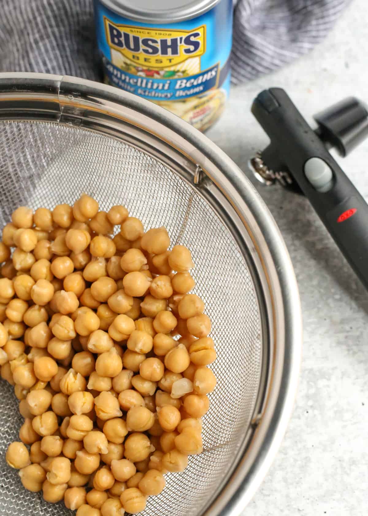 A colander with dried chickpeas next to an unopened can of beans and can opener, indicating that rinsing canned foods can be one way to reduce sodium for a low sodium diet for heart health