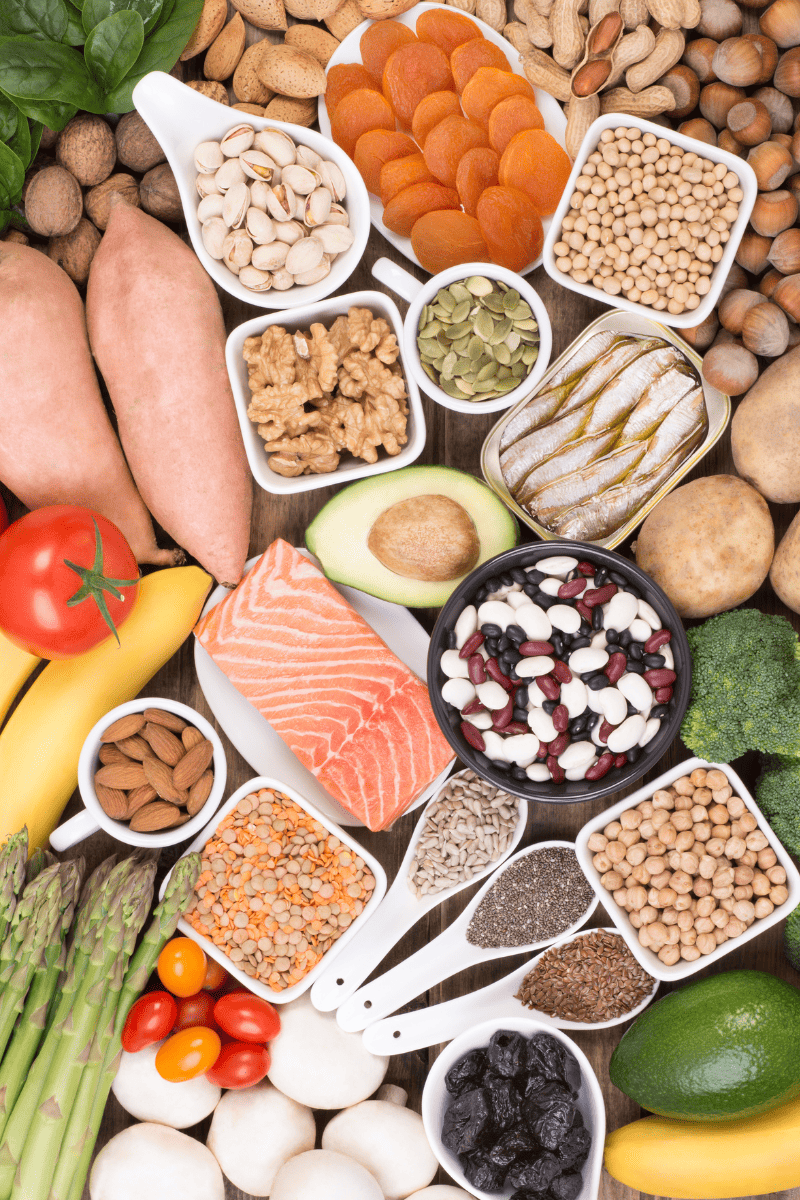 A colorful flat lay of potassium rich foods including salmon, bananas, dried apricots, pistachios, walnuts, dried beans and legumes, sweet potatoes, prunes, and lentils that can be included in a low sodium diet for heart health