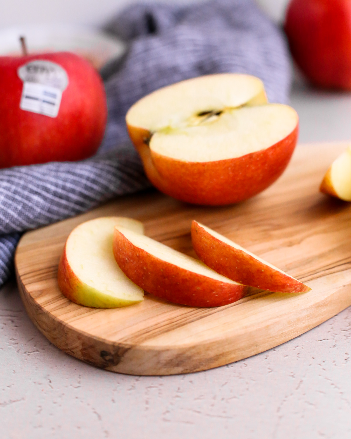 Close up view of an Envy apple sliced in half, showing a crisp white interior that stays fresh and flavorful longer, arranged on a wooden cutting board with more apples in the background