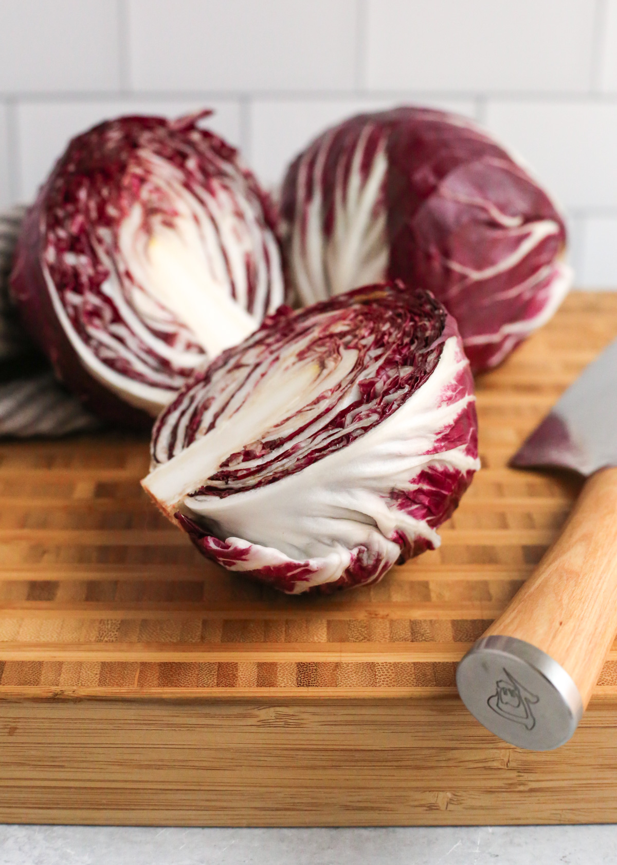 Two heads of radicchio on a butcher block cutting board, with one sliced in half to reveal the inner leaves and marbling of deep red and white colors