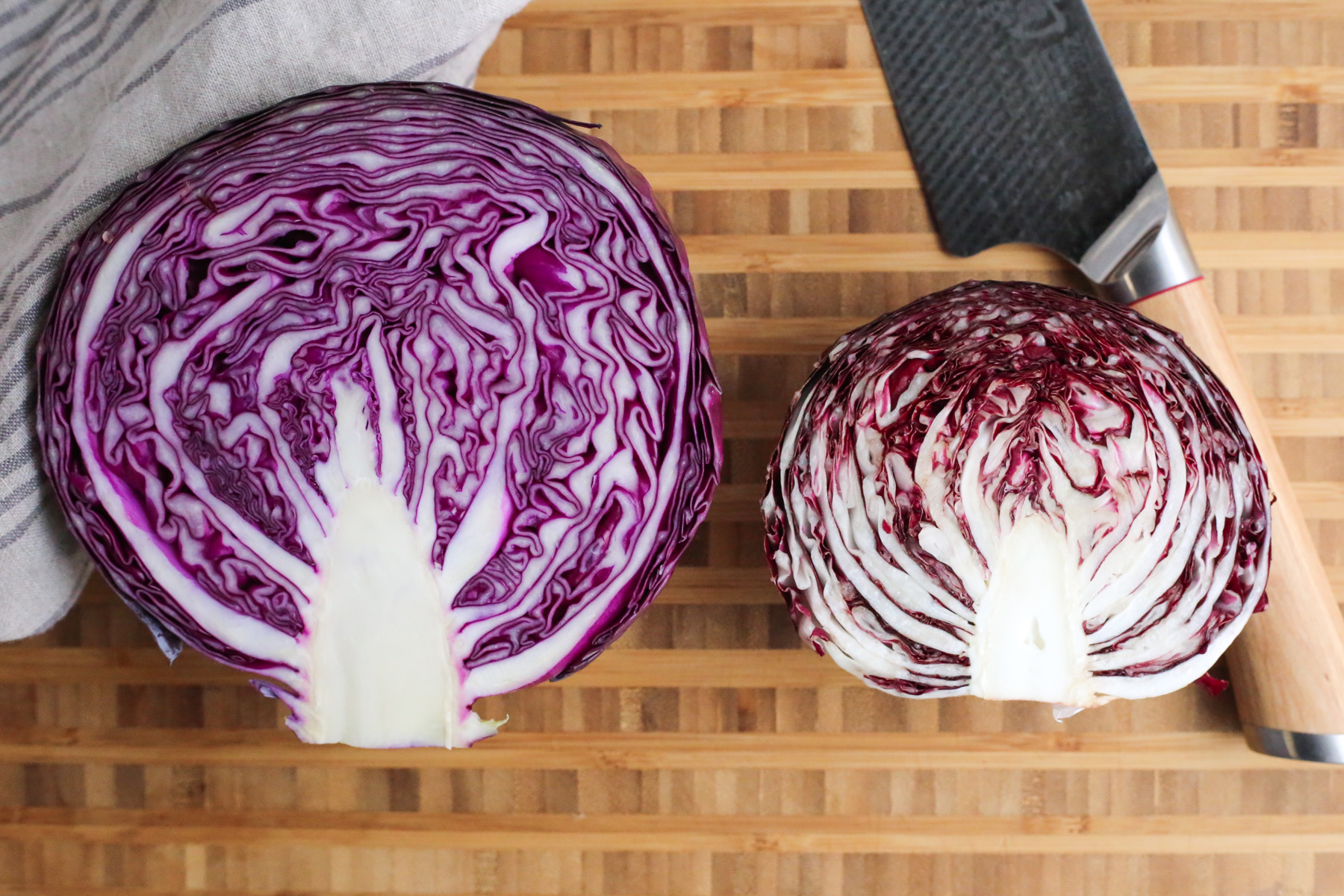 Overhead view of a butcher block cutting board with a head of red cabbage and radicchio sliced in half to reveal the cross-sectional view, comparing the difference between the two 