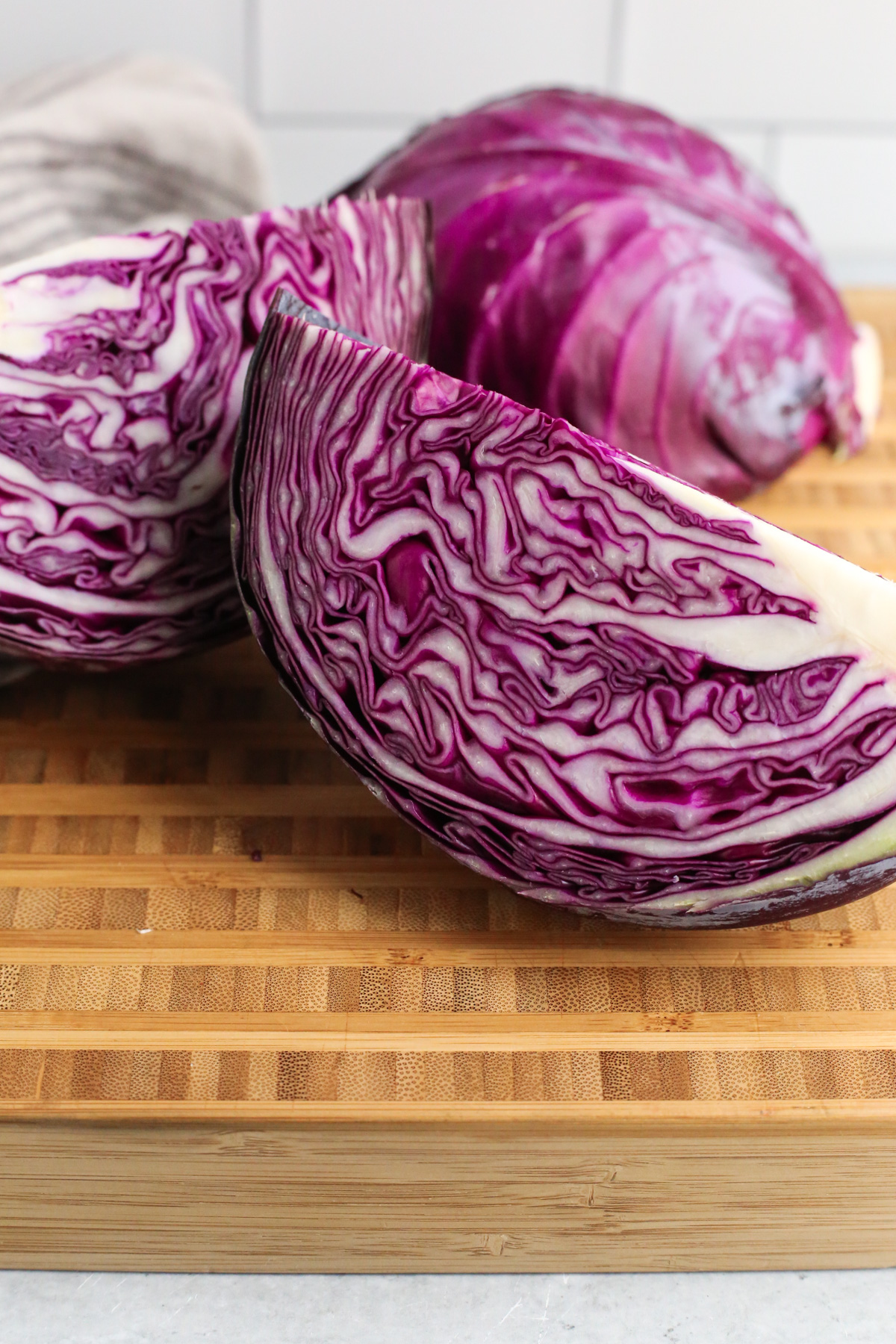 Several pieces of sliced red cabbage on a butcher block cutting board, revealing the densely packed, vibrantly colored leaves and white core
