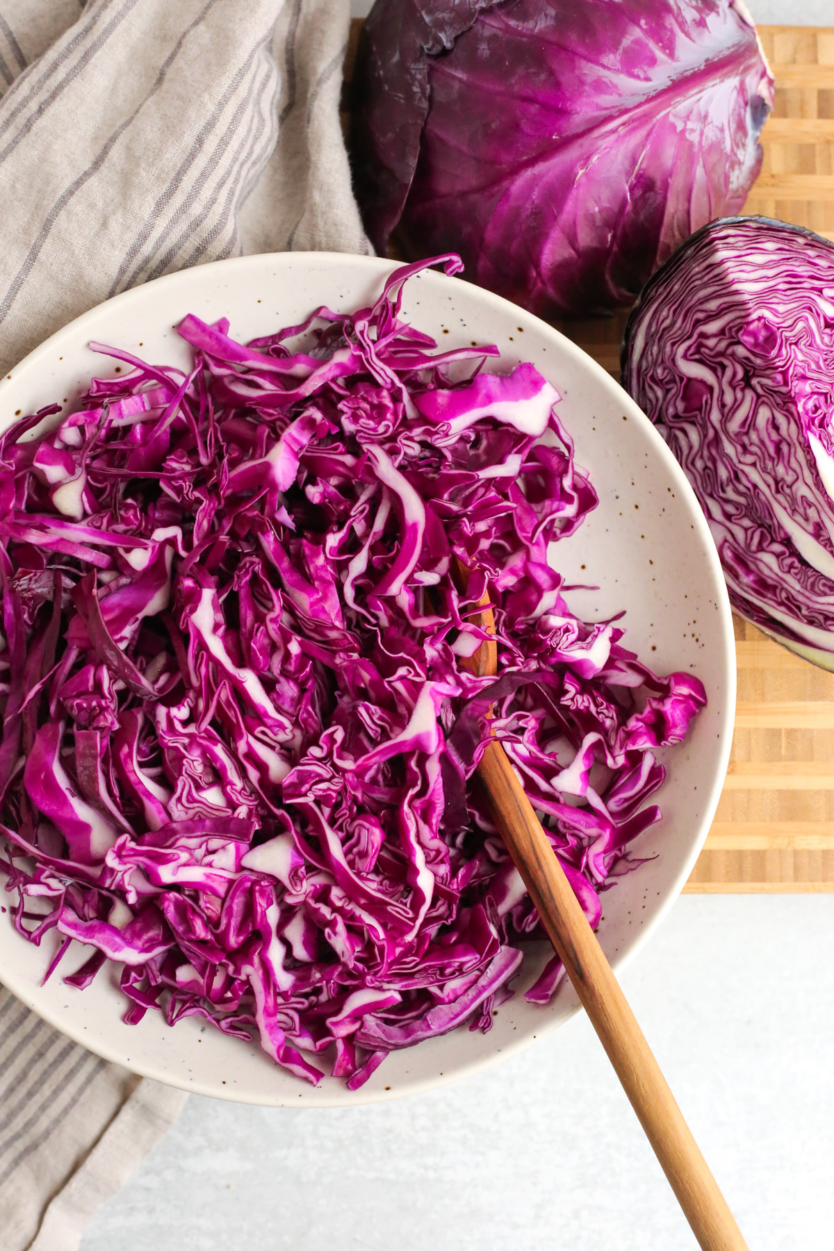 Overhead view of a large salad bowl filled with finely sliced and shredded red cabbage, with a wooden serving spoon arranged on the side of the bowl