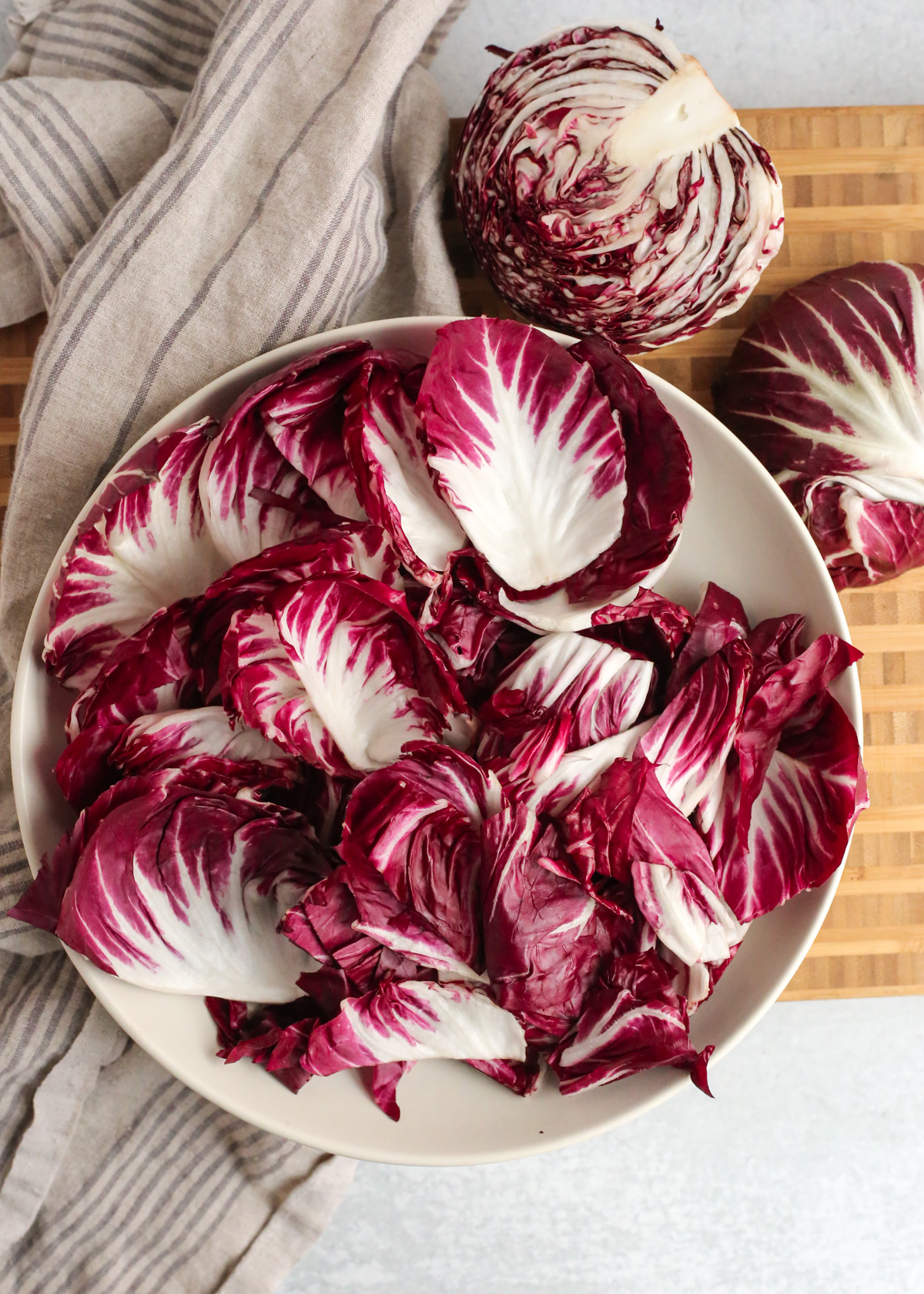Overhead view of a large salad bowl filled with leaves of radicchio, arranged near another head of radicchio that is sliced in half