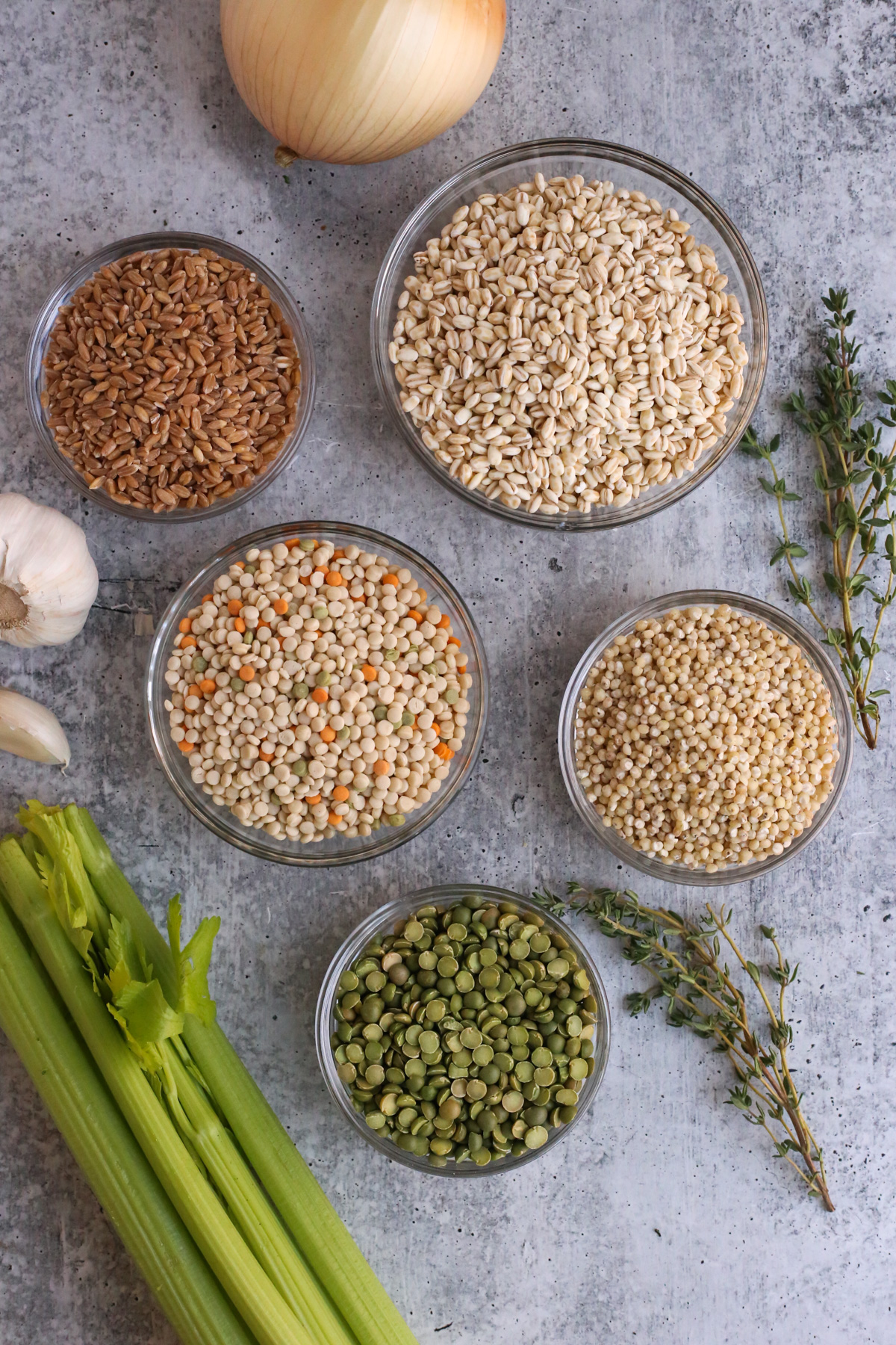 Comparison of various grains displayed in small ramekins, including pearled couscous, barley, farro, pearled sorghum, and green split peas