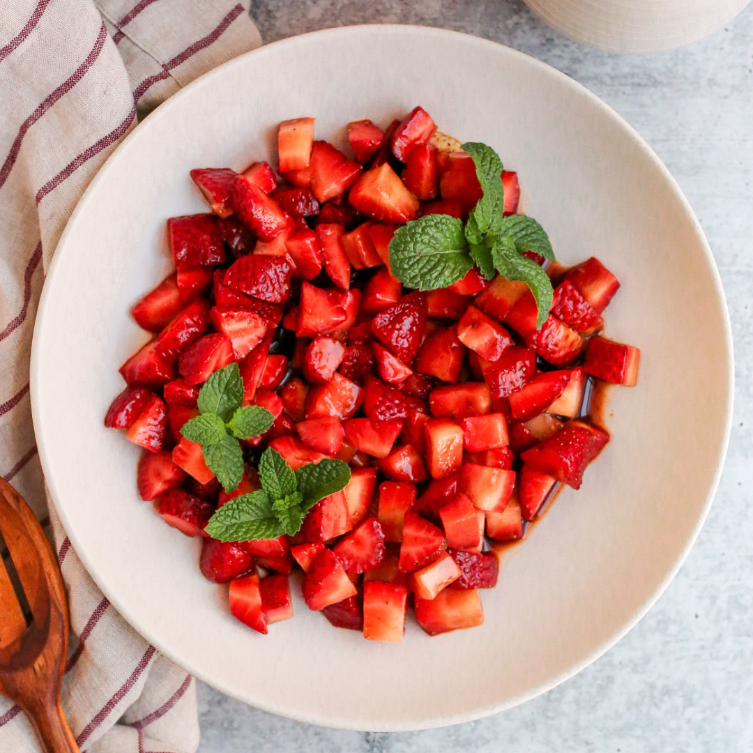 Overhead view of a bowl of balsamic macerated strawberries, garnished with a few sprigs of fresh mint.