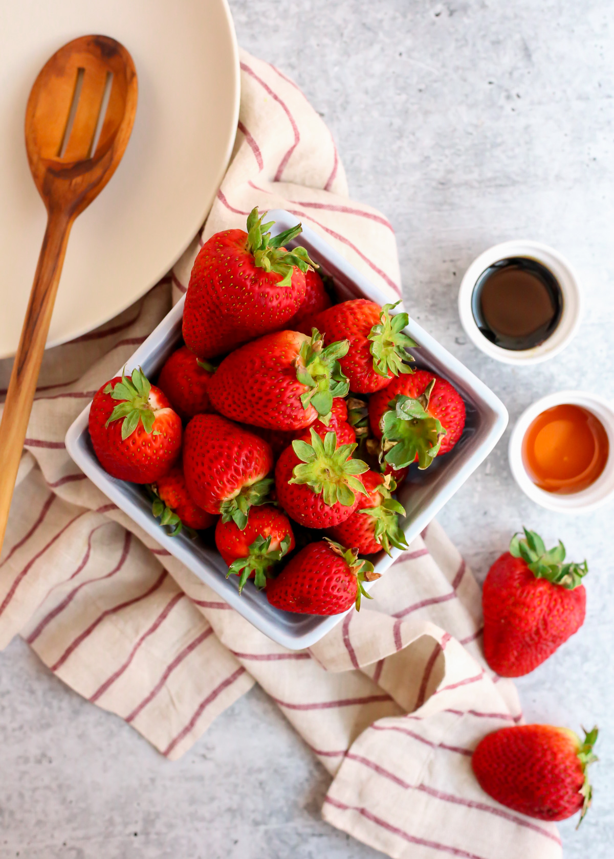Flatlay style image of the ingredients needed to make balsamic macerated strawberries, including fresh strawberries, balsamic vinegar, and honey