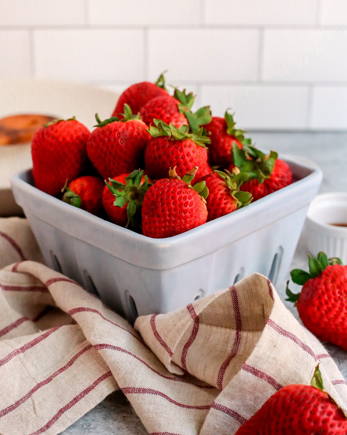 Fresh strawberries with green stems displayed in a ceramic carton on a kitchen countertop