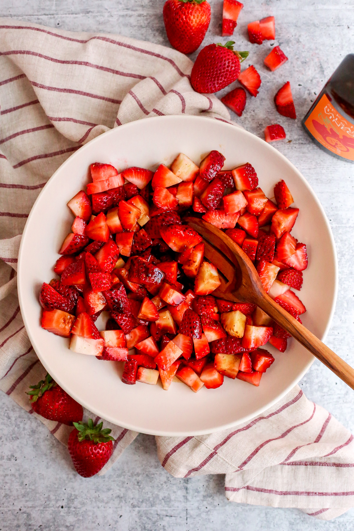 A large mixing bowl filled with chopped fresh strawberries, drizzled lightly with balsamic vinegar.
