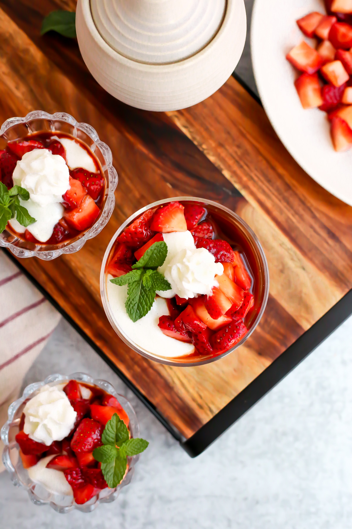 Overhead view of a serving platter with small glass dishes filled with strawberries and cream. A small sprig of fresh mint decorates the side of each dish along with a dollop of fresh whipped cream