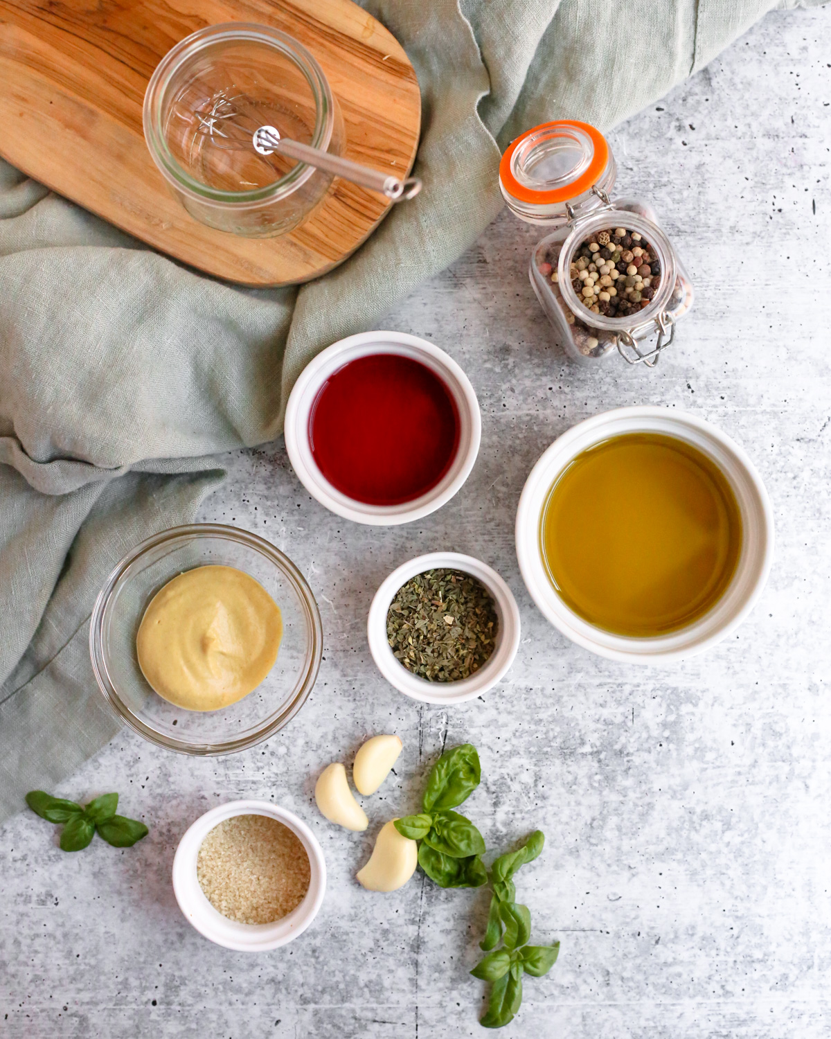 Flatlay style image of all the ingredients needed to make a homemade red wine vinaigrette dressing recipe, displayed on a kitchen countertop in various sizes of small glass dishes or ramekins