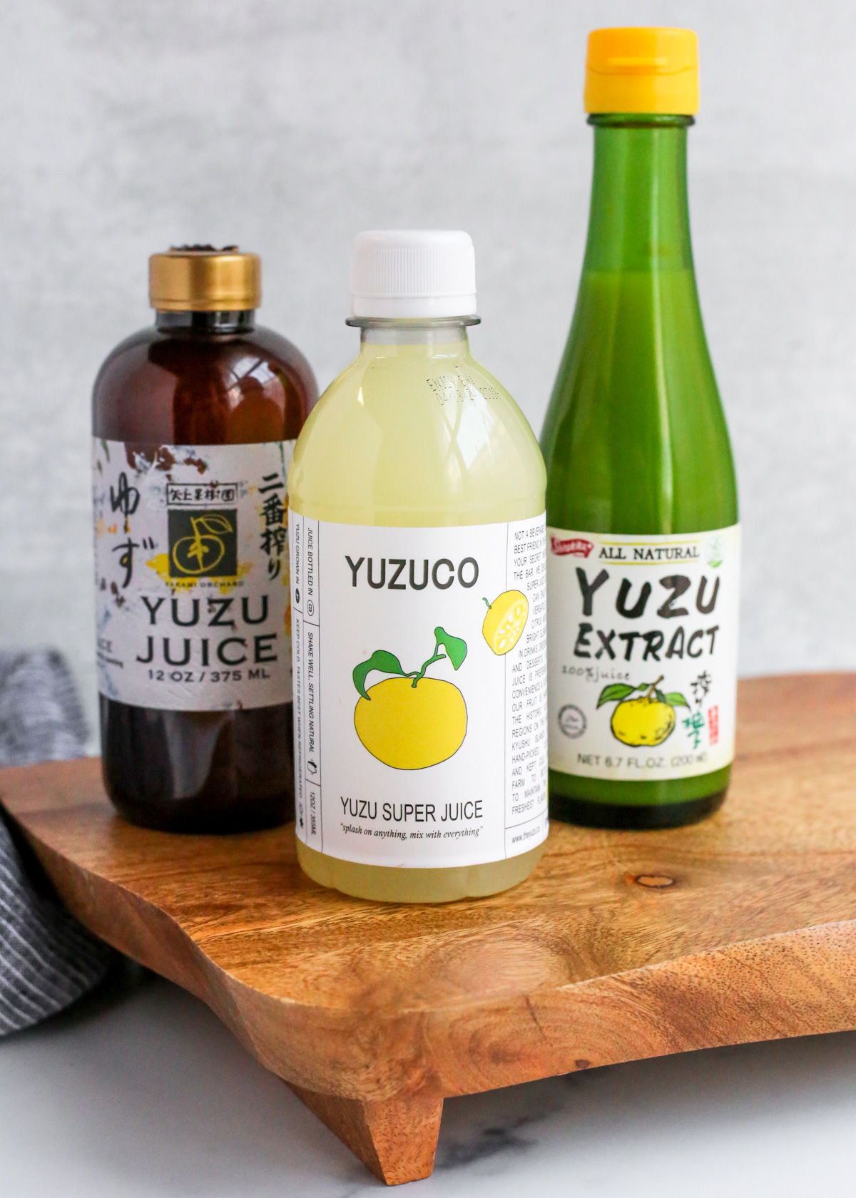 A wooden serving board displays three bottles labeled as yuzu juice, yuzu super juice, and all-natural yuzu extract