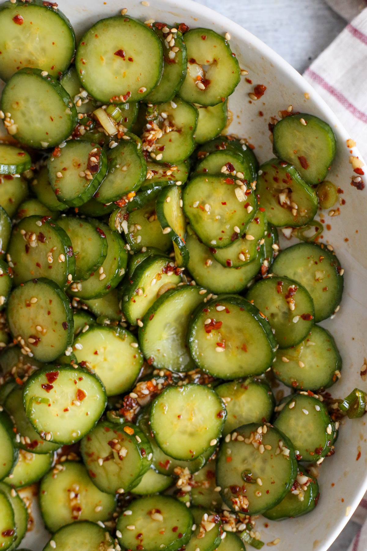 Overhead view of a large serving or mixing bowl filled with sliced cucumbers, seasoned with a light sauce mixture to make oi muchim or spicy Korean cucumber salad