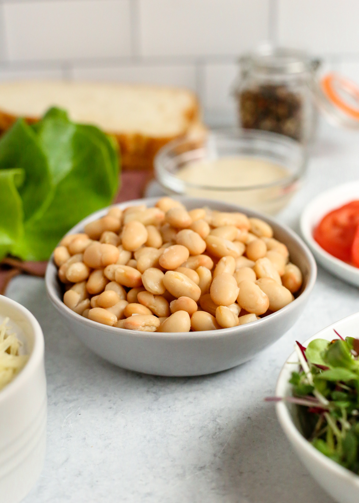 A close up shot of canned white beans that have been drained and rinsed, alongside the other ingredients for caesar beans on toast in the background