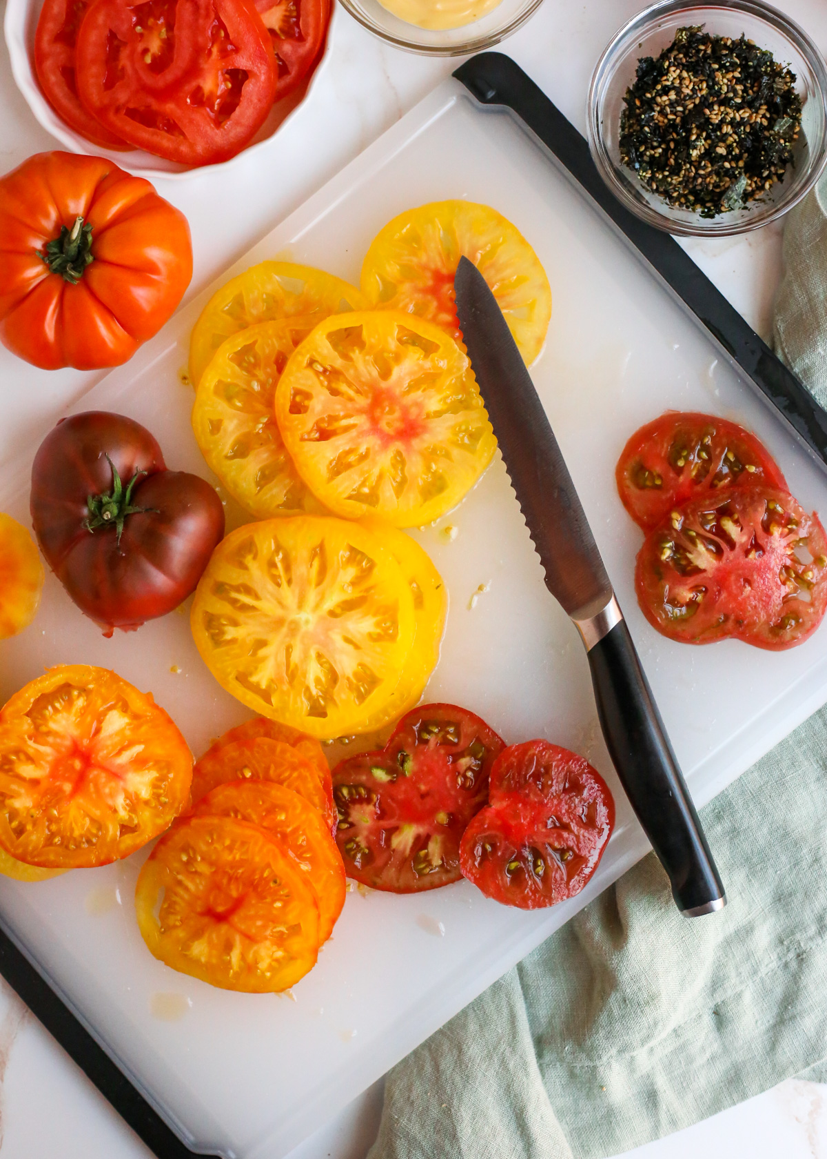 Overhead view of a cutting board and serrated knife with partially chopped and sliced heirloom tomatoes in varying shades of red, orange, and yellow