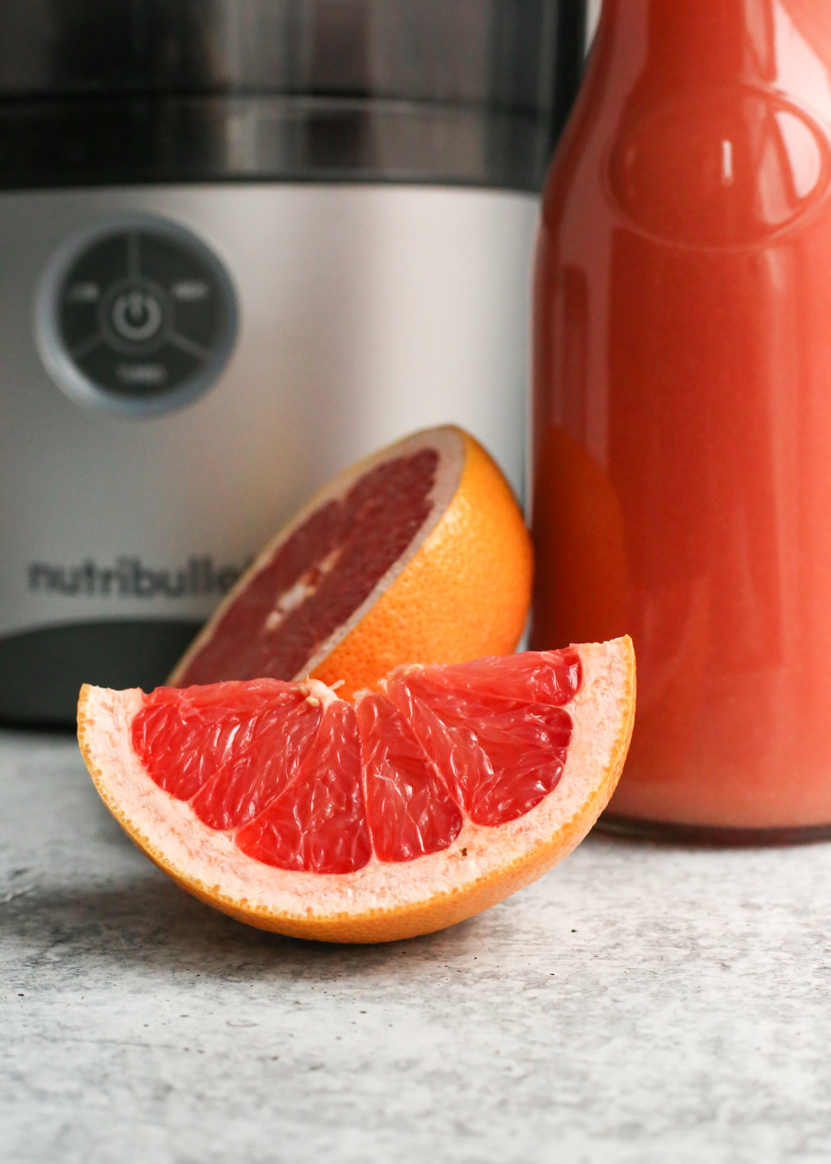 A close up shot of a wedge of grapefruit sitting in front of a juicing machine on a kitchen countertop, revealing the juicy segments that are richly colored in a bright, vibrant red hue