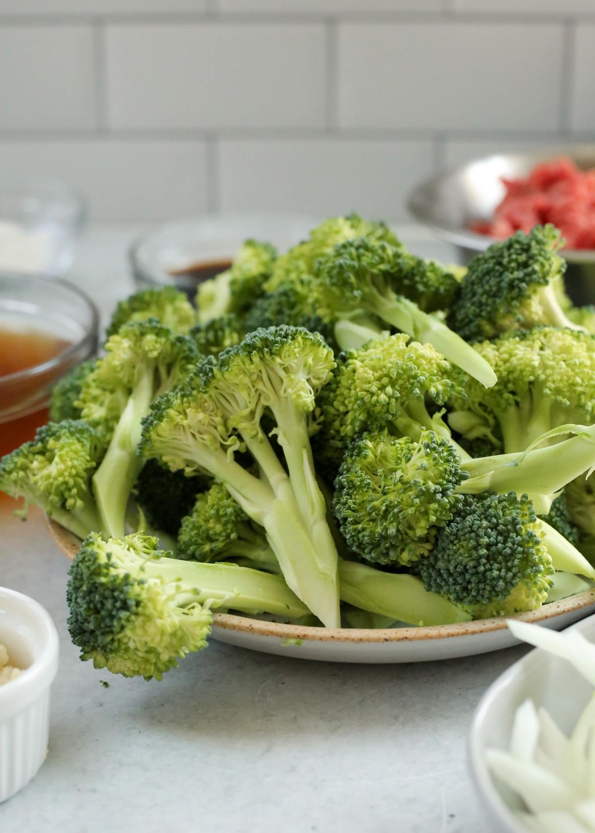 A close up side view of fresh broccoli florets, stacked high on a ceramic dish in a kitchen setting