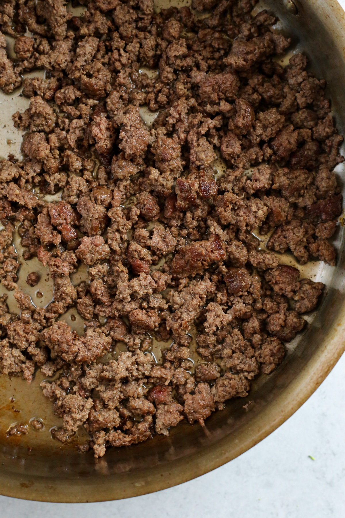 Ground beef browning in a large stainless steel skillet. 