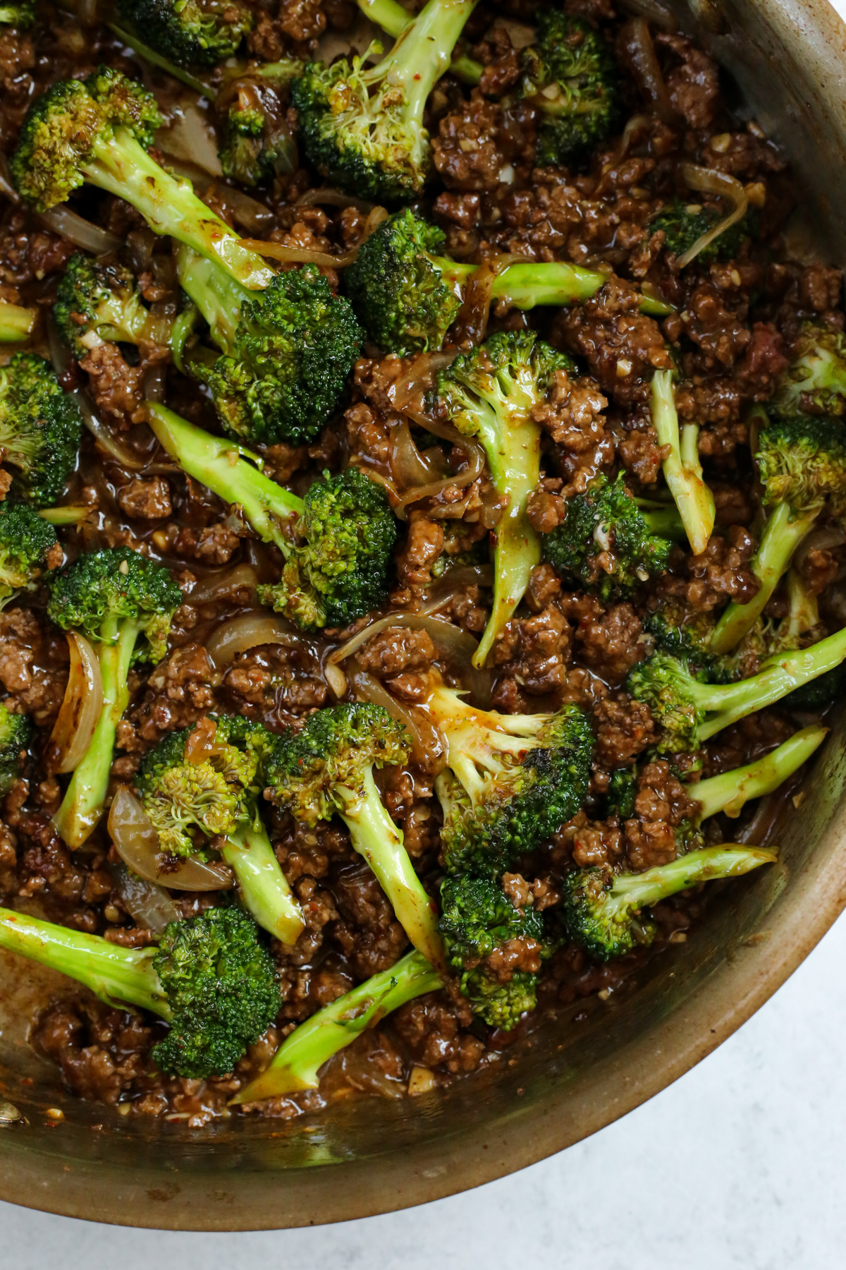 A large stainless steel skillet containing a freshly made batch of ground beef and broccoli, all coated in a rich, savory brown sauce.