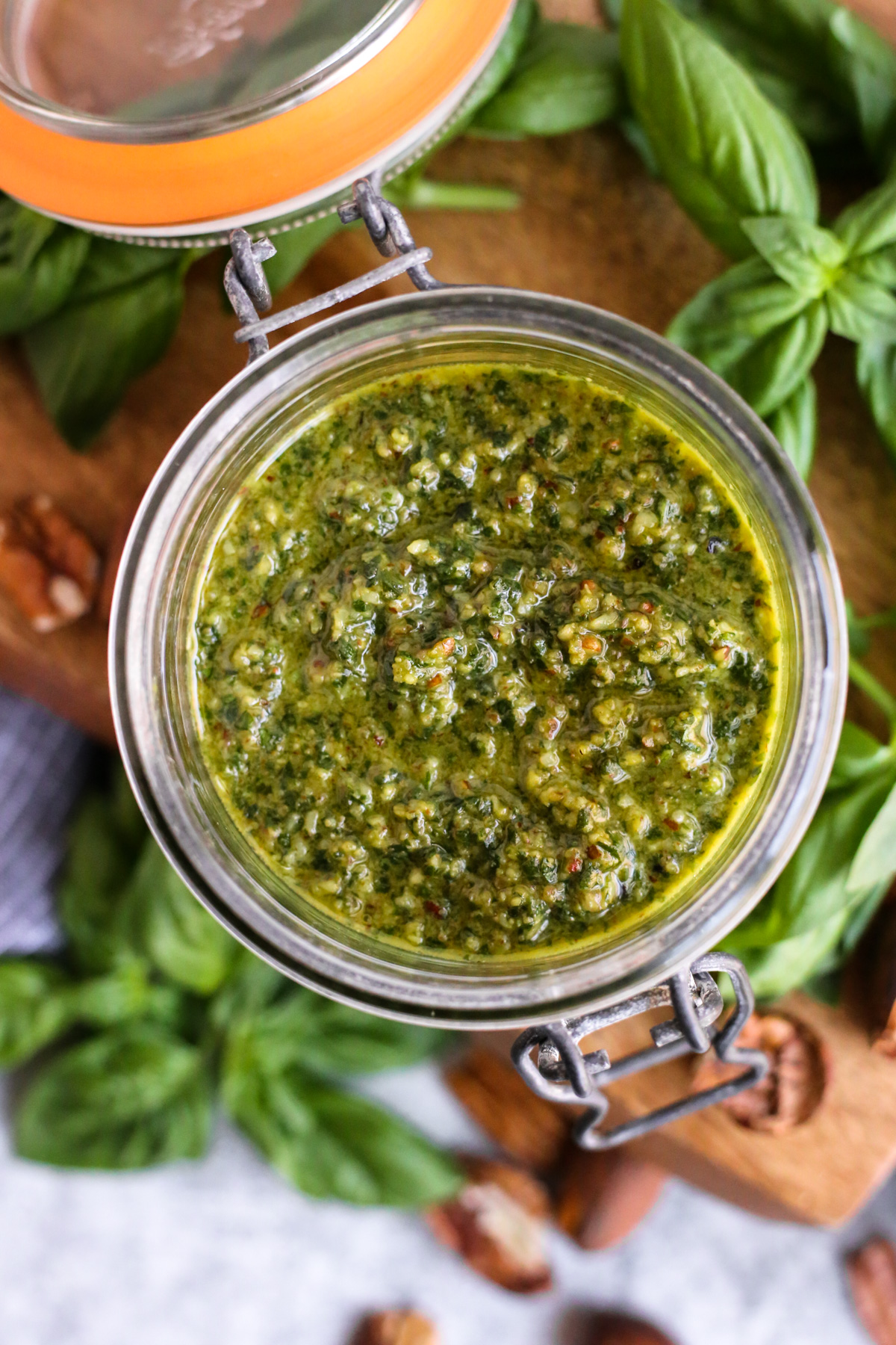 Overhead view of a homemade pecan pesto recipe, stored in a glass jar with an opened lid to display the bright green sauce with small chunks of pecans visible 