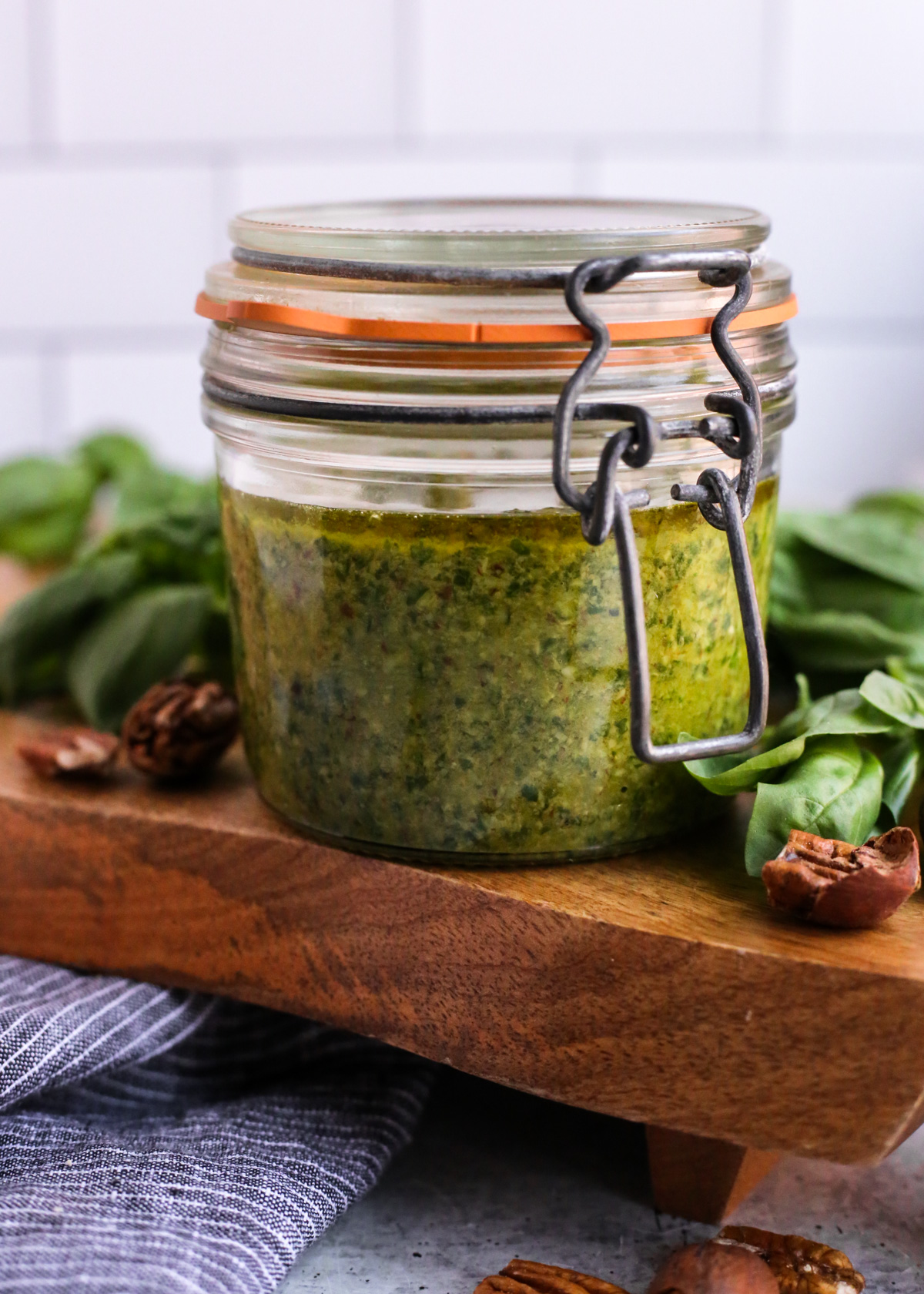 A side view of the glass strange container for the pecan pesto, showing the thick layer of vibrant green pesto covered with a thin layer of golden olive oil to prevent browning 