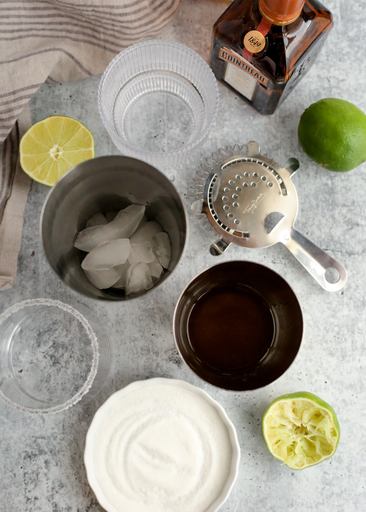 Overhead view of a cocktail shaker showing ice cubes in one half and the measured ingredients for a yuzu margarita cocktail in the other