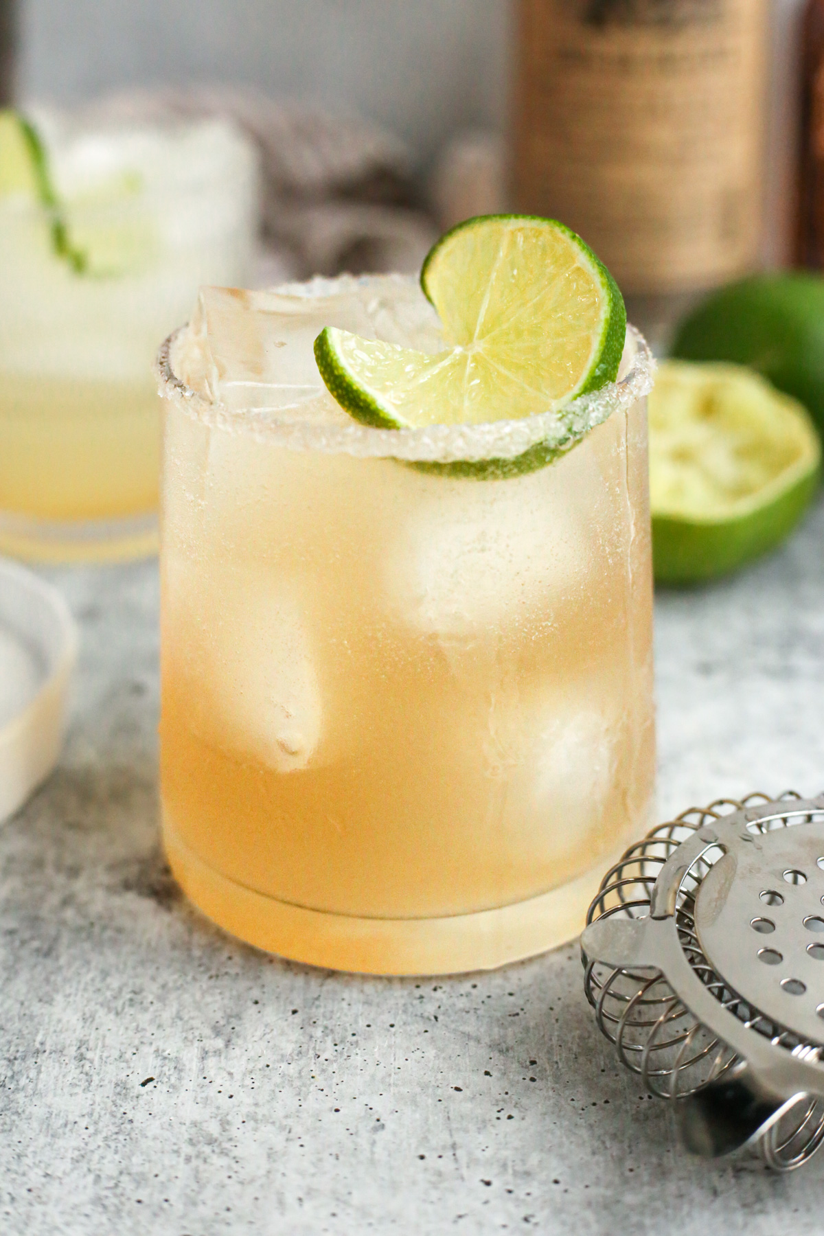 A yuzu margarita is served in a clear glass, rimmed with sugar, and garnished with a lime wheel. The drink looks chilled and refreshing