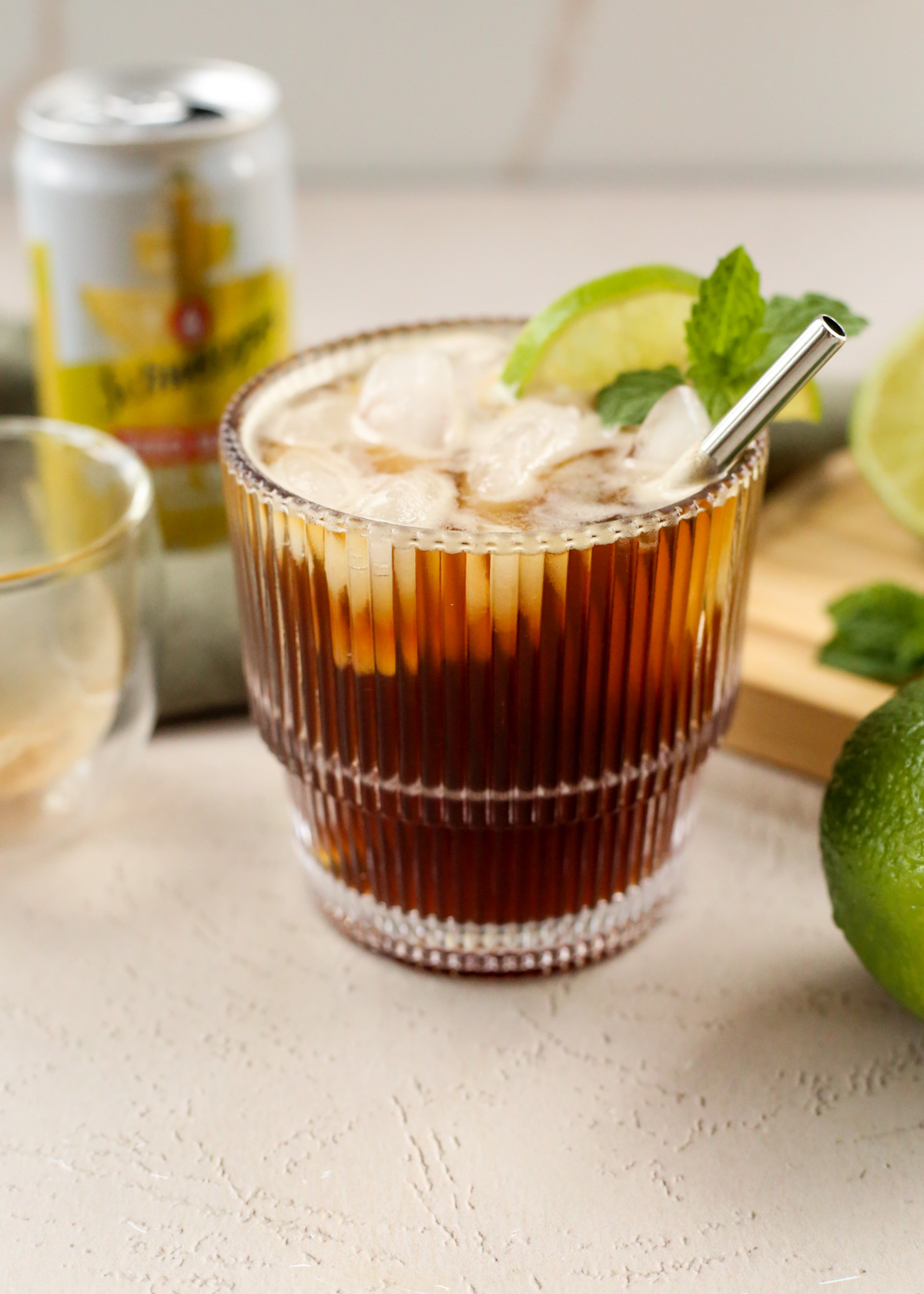 A clear glass filled with espresso and tonic with ice cubes and garnished with a slice of lime and sprig of mint