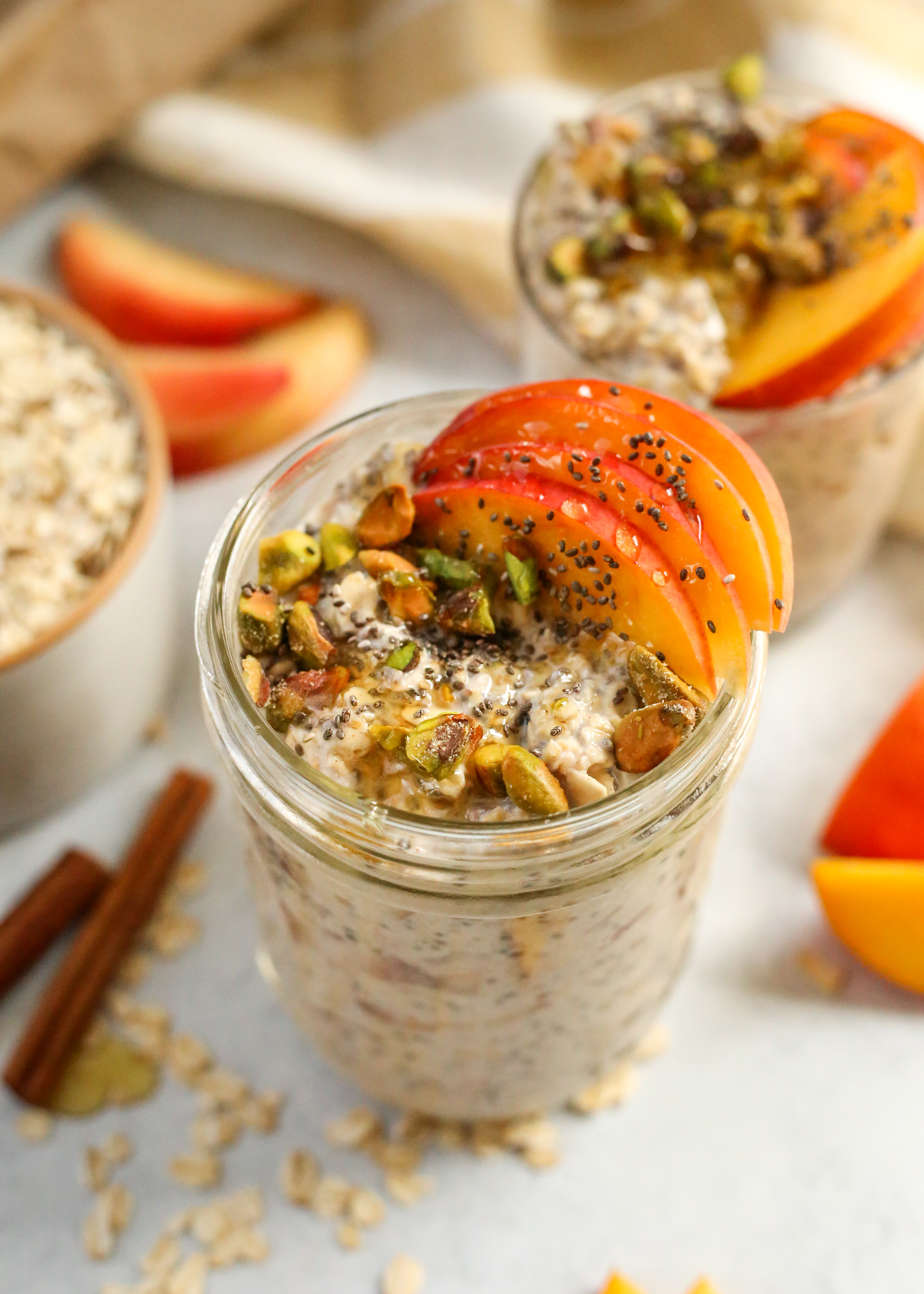 A mason jar filled to the top with peaches and cream overnight oats, topped with extra peaches, roasted pistachios, chia seeds, and honey