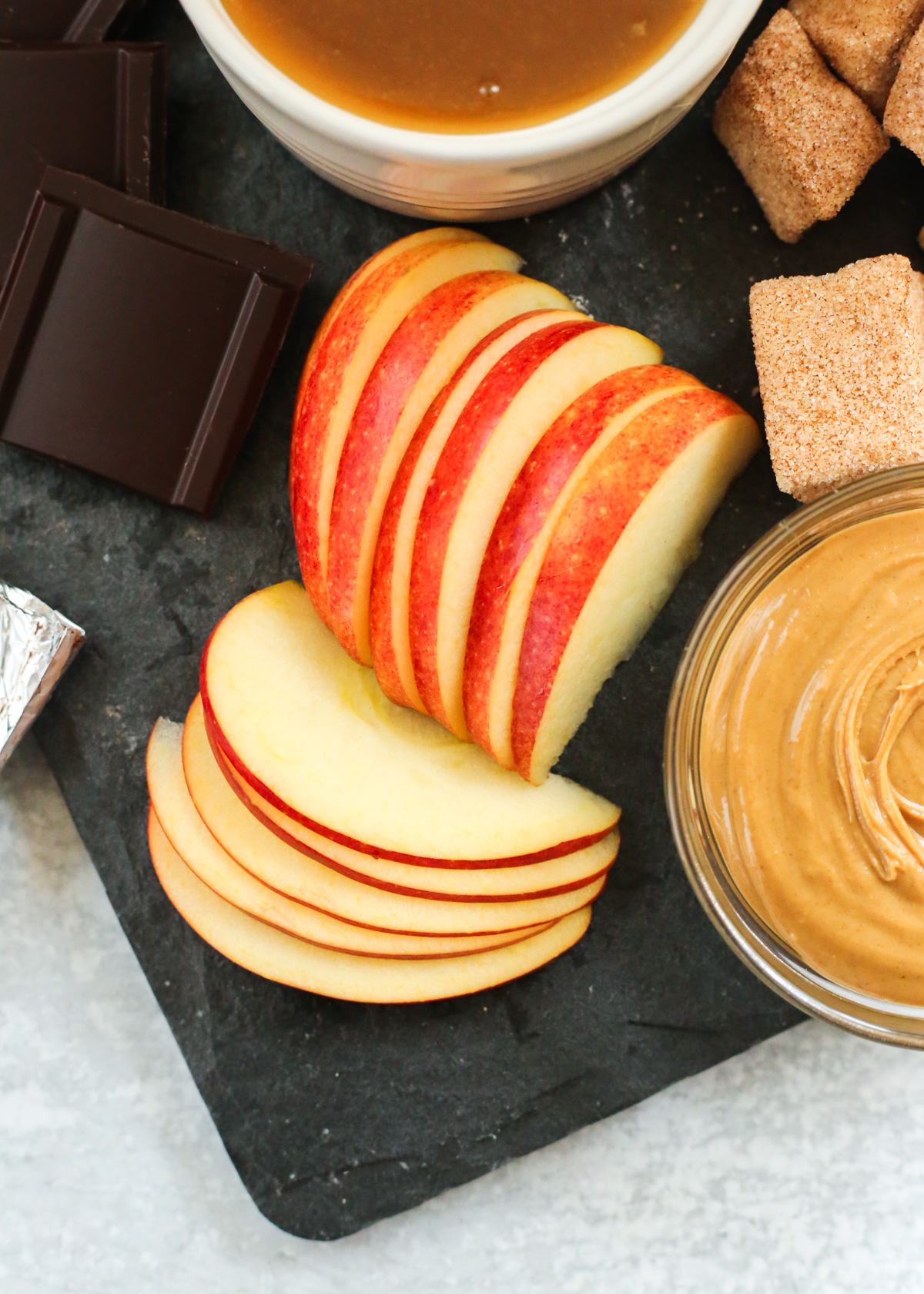 Overhead shot of sliced apples, arranged on a dessert board made of dark grey slate, angling in opposite directions to reveal the bright, crisp flesh and the vibrant red skin.