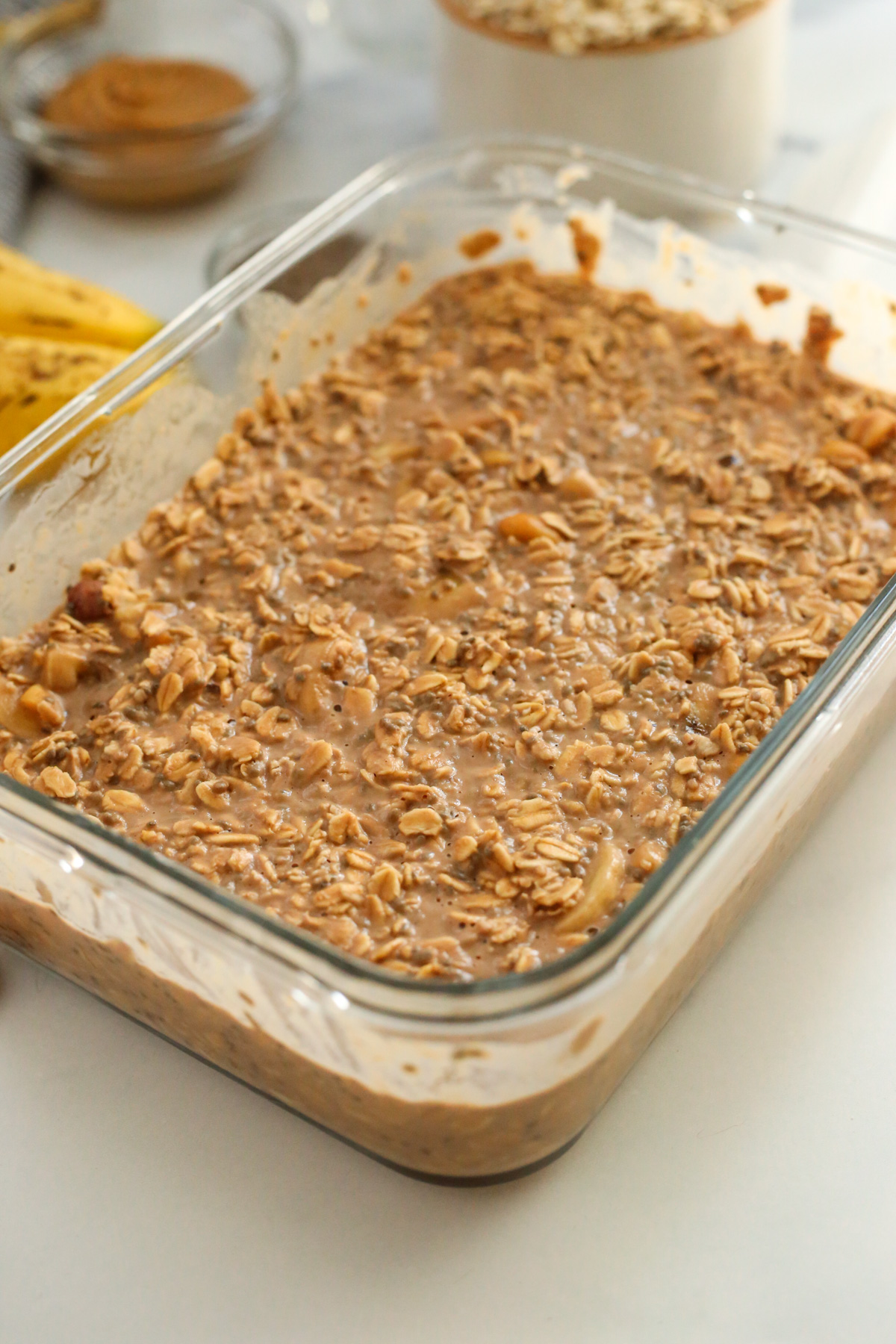 A view into a large storage container holding a batch of chocolate overnight oats, which appear thick and creamy but not as aesthetically pleasing as the styled images of individual portions with garnishes