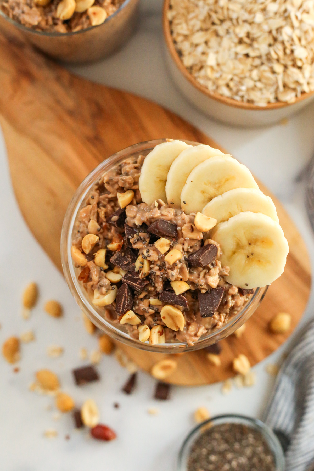 A top-down view into a mason jar full of overnight oats topped with pieces of peanuts and chocolate chunks, as well as five uniform slices of ripe banana