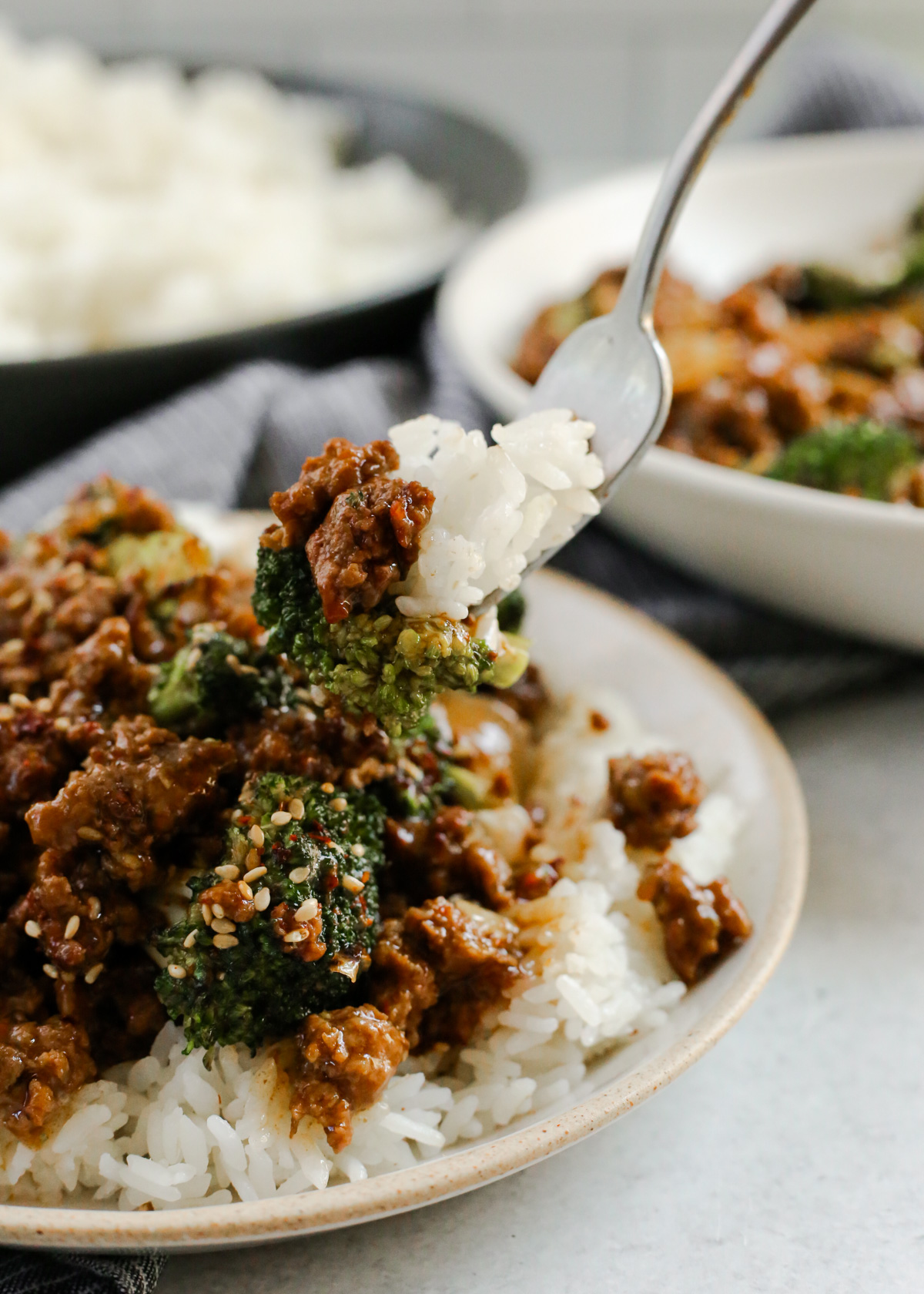 A silver forks descends into a plate of steamed white rice covered with ground beef and broccoli