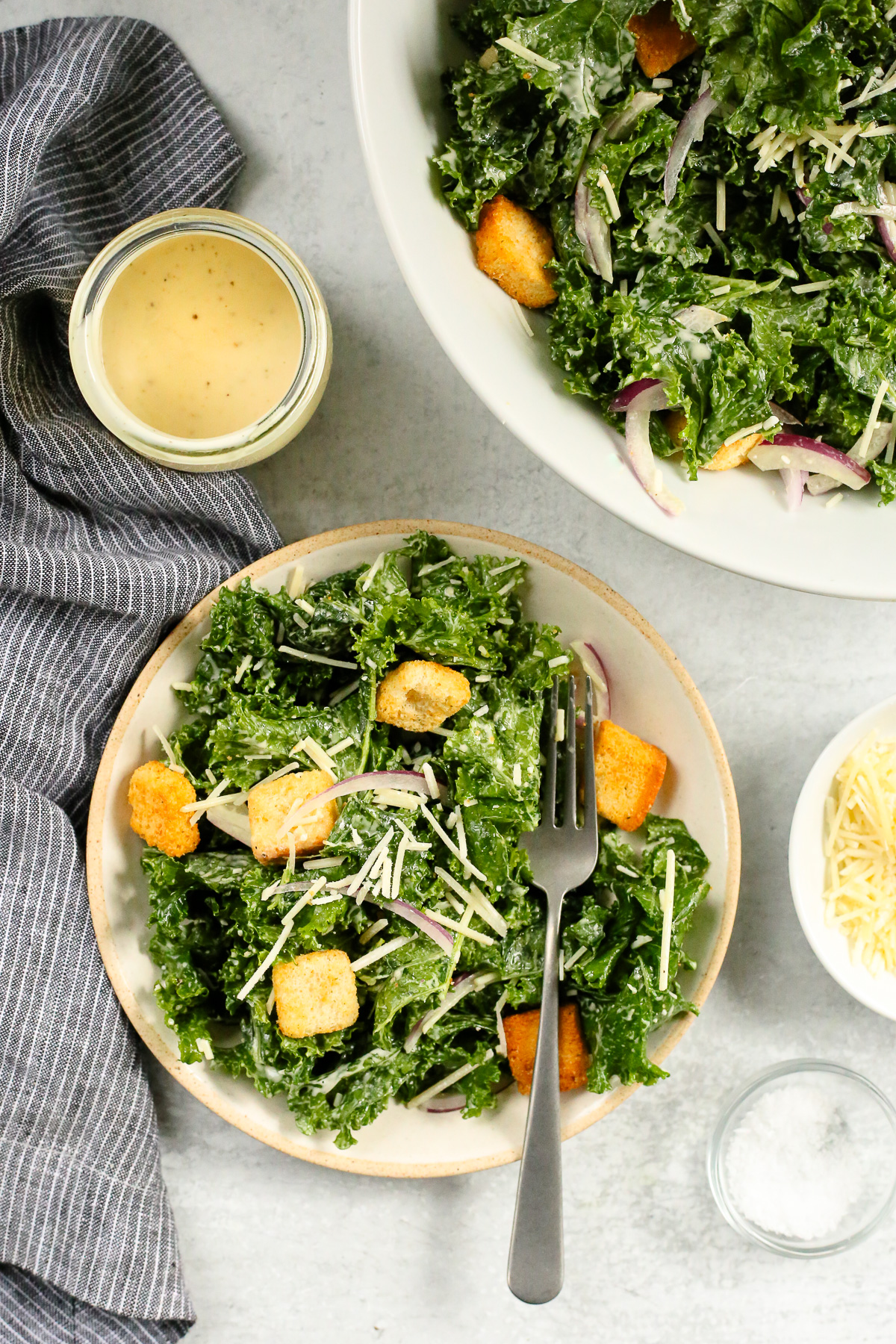 Overhead view of a salad plate piled high with a massaged kale caesar salad, topped with crunchy croutons with a silver fork arranged on the side of the plate.