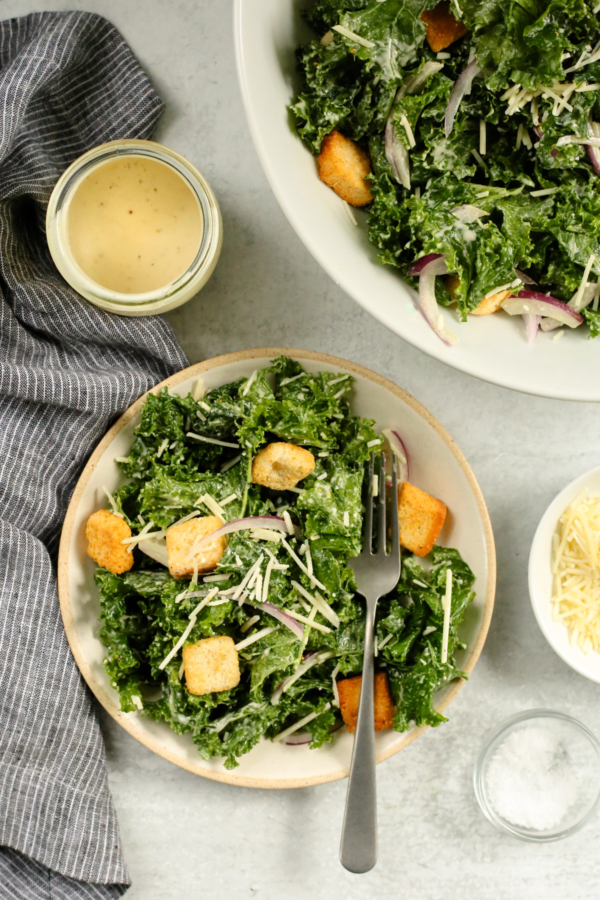 Overhead view of a salad plate piled high with a massaged kale caesar salad, topped with crunchy croutons with a silver fork arranged on the side of the plate