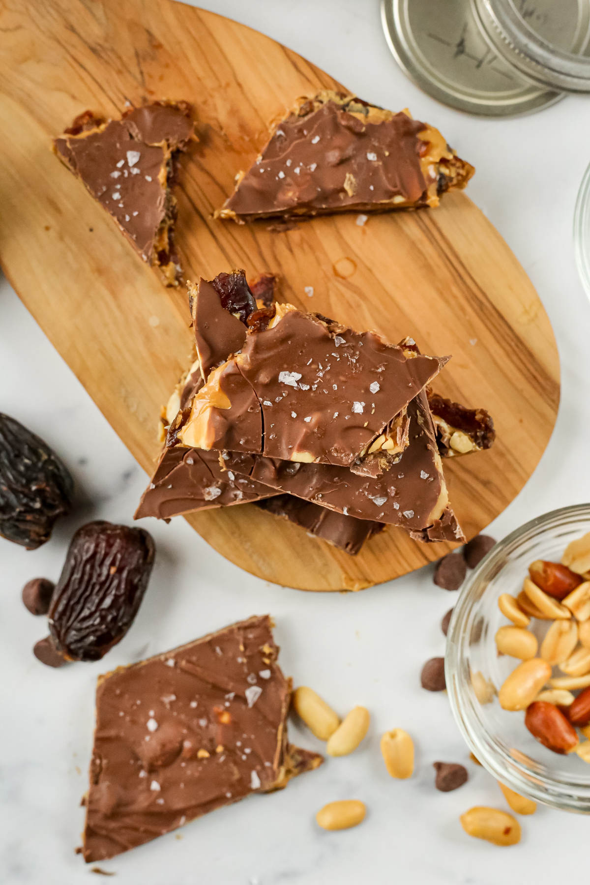 Overhead view of a stack of date bark displayed on a small wooden serving board, with various ingredients and medjool dates scattered nearby