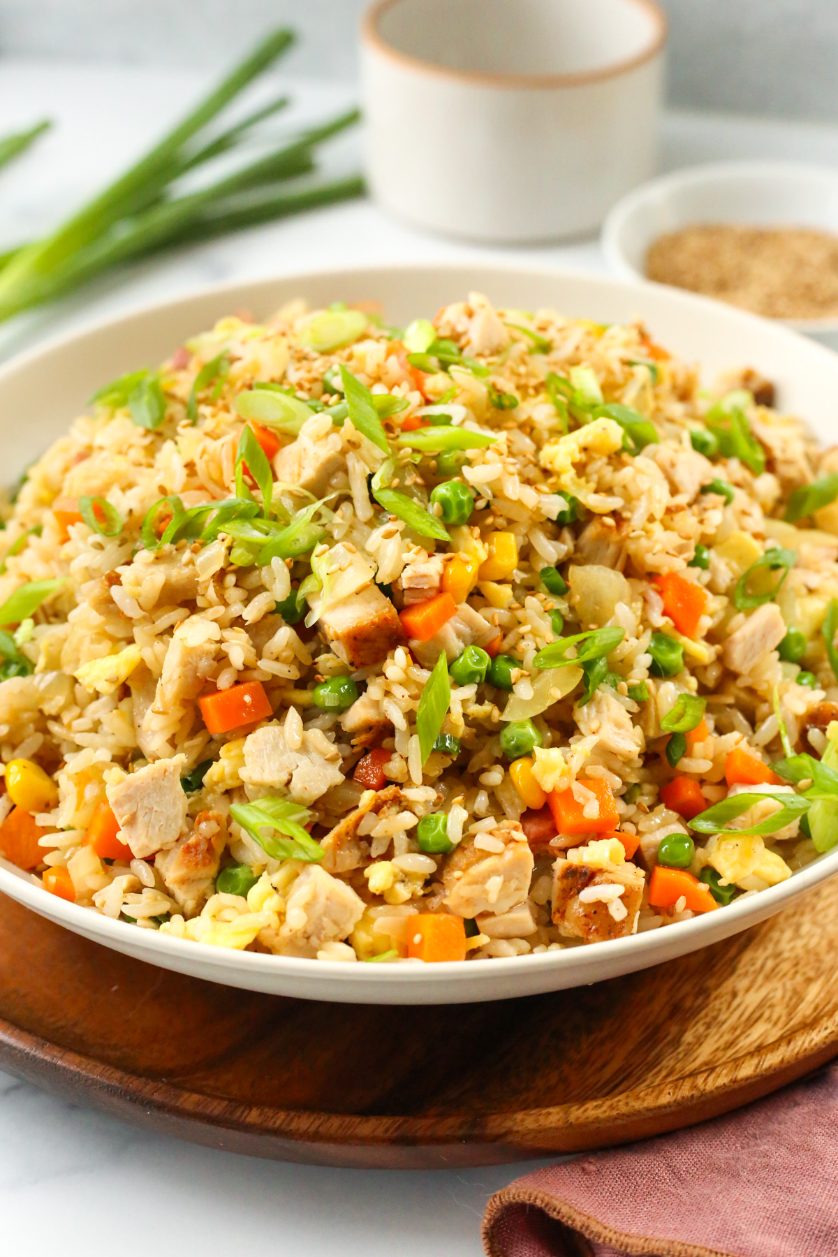 An angled view into a large white serving bowl filled with fried rice, with visible chunks of leftover turkey, green onions, green peas, carrots, corn, and onions with a few toasted sesame seeds sprinkled on top