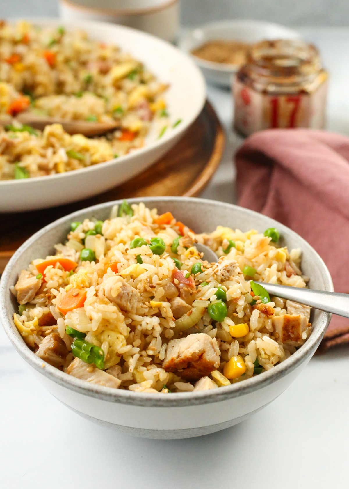 A serving of leftover turkey fried rice is displayed in a small grey ceramic bowl with a spoon nestled into one side, with the rest of the fried rice in a larger bowl in the background